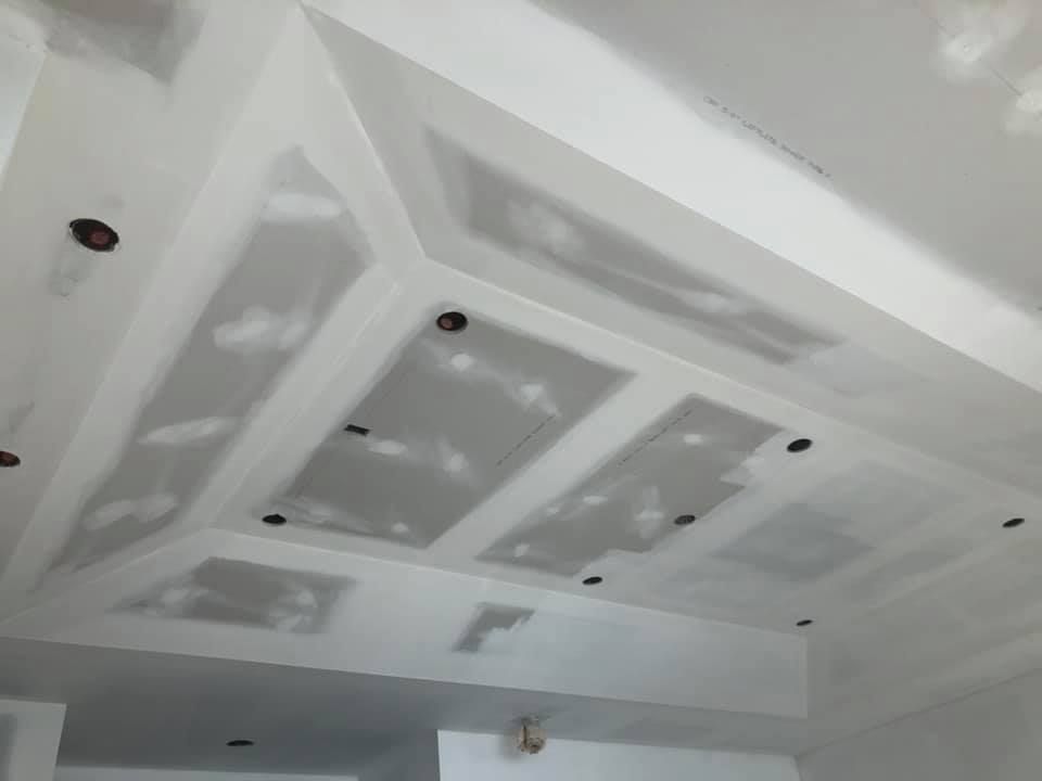 Unfinished ceiling with recessed lighting cutouts and drywall taped and patched with white joint compound.
