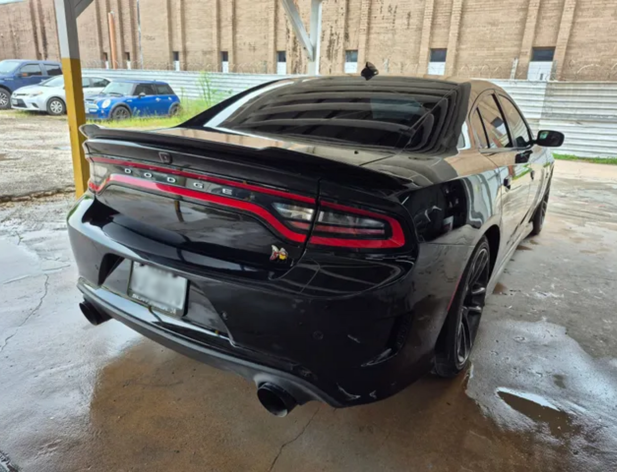 Black sports sedan parked under a carport, rear view on a snowy day
