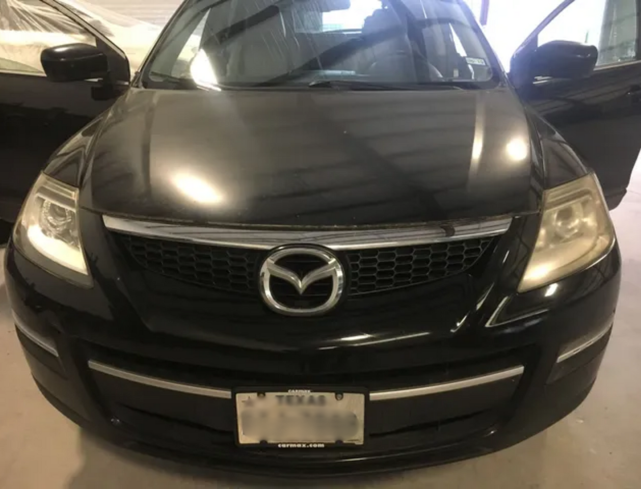 Front view of a black Mazda sedan parked indoors, with headlights on and a Texas license plate.
