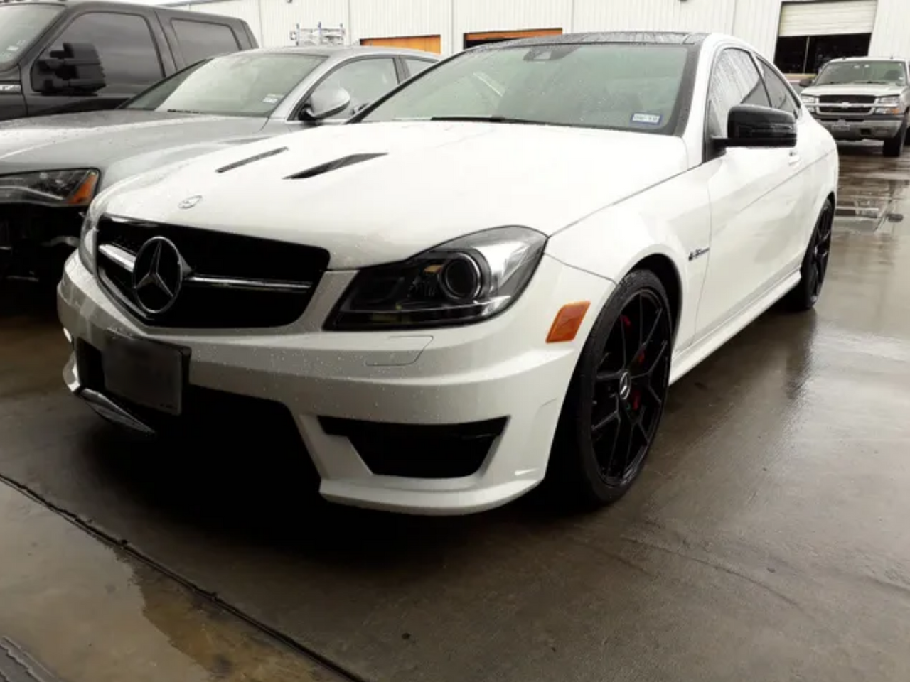 White Mercedes-Benz coupe parked indoors on a wet floor, viewed from the front left.