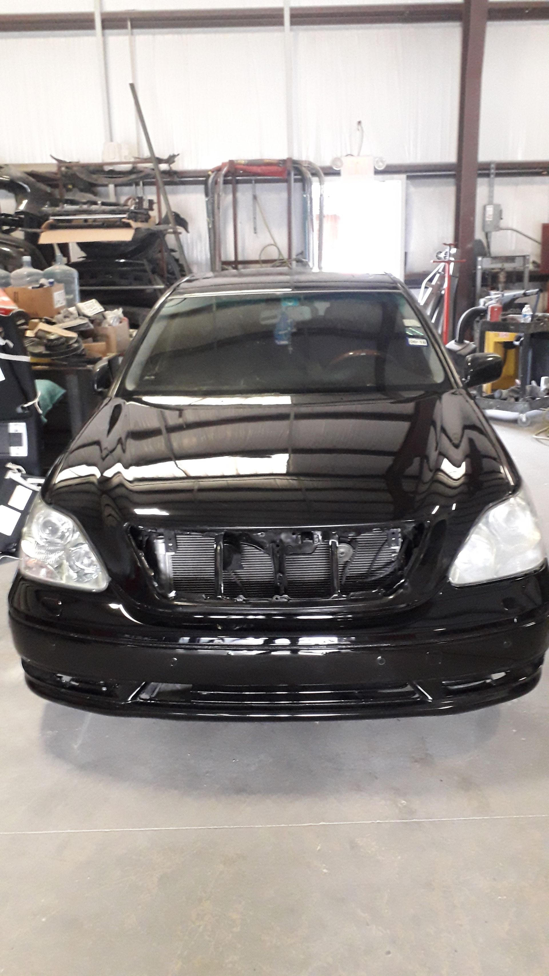Black sedan parked in a garage with its front grille removed, surrounded by tools and equipment.