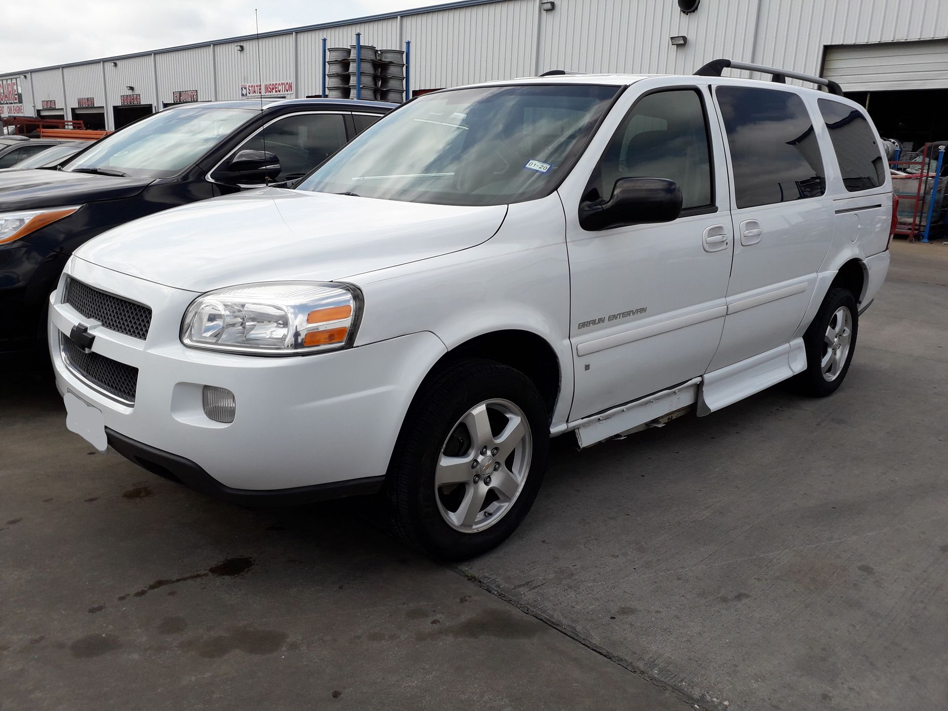 White minivan parked in a lot beside other vehicles and a warehouse building
