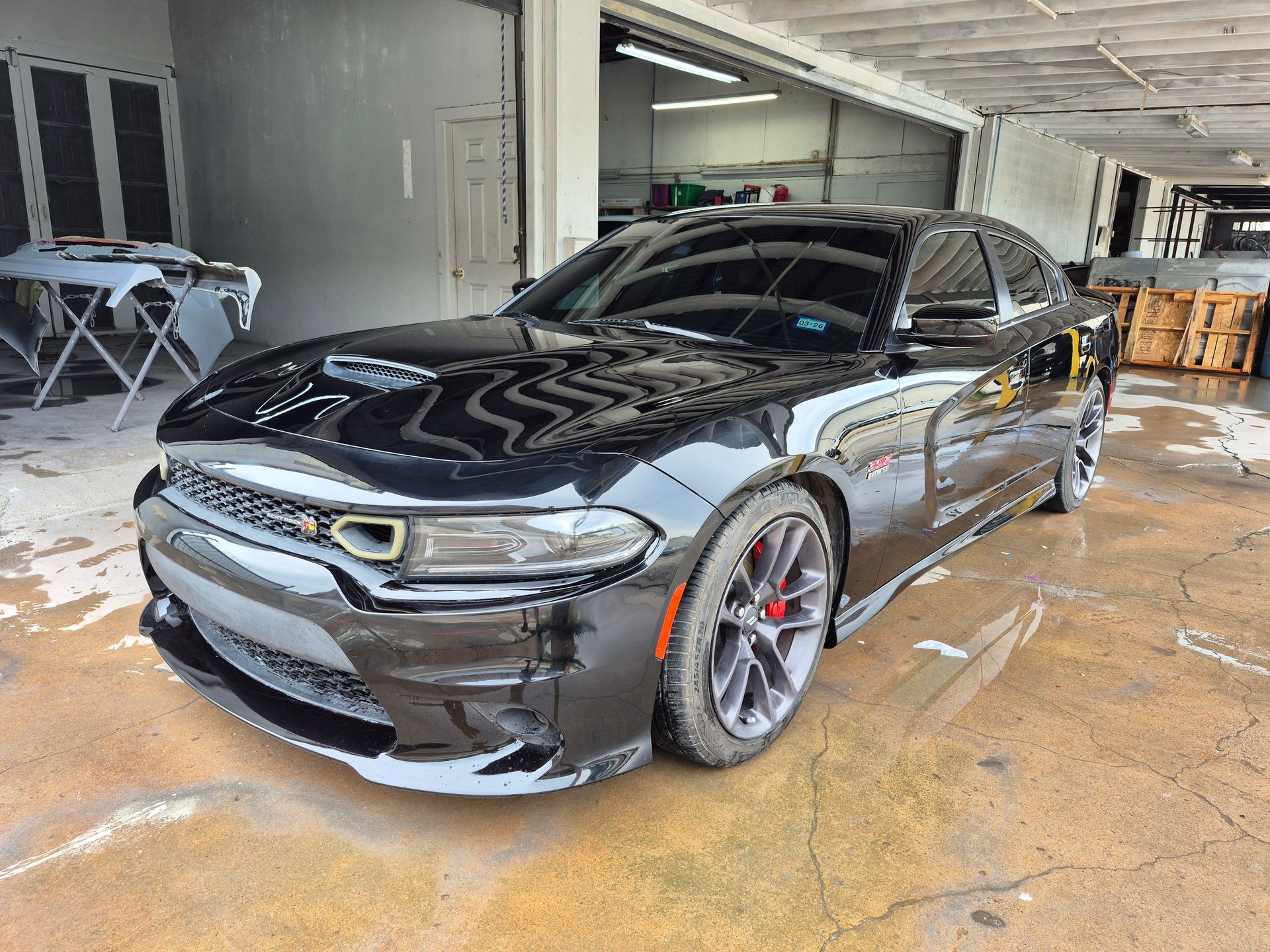 Black sports car parked in a garage, front-left view with glossy finish and gray wheels