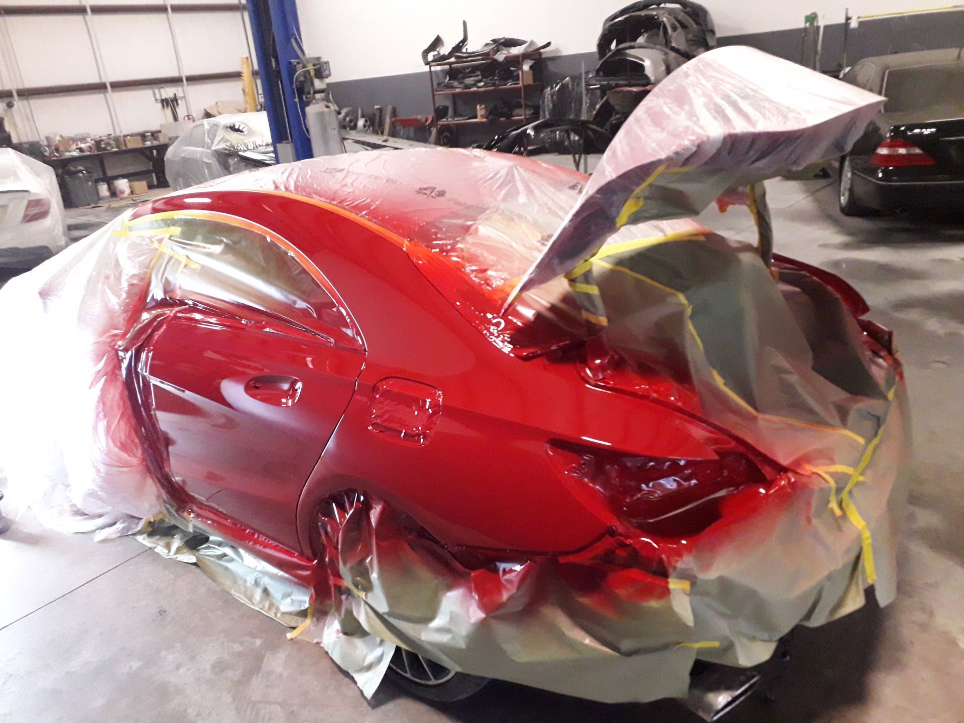 Red sports car in a body shop, wrapped in plastic and masked for paint work.