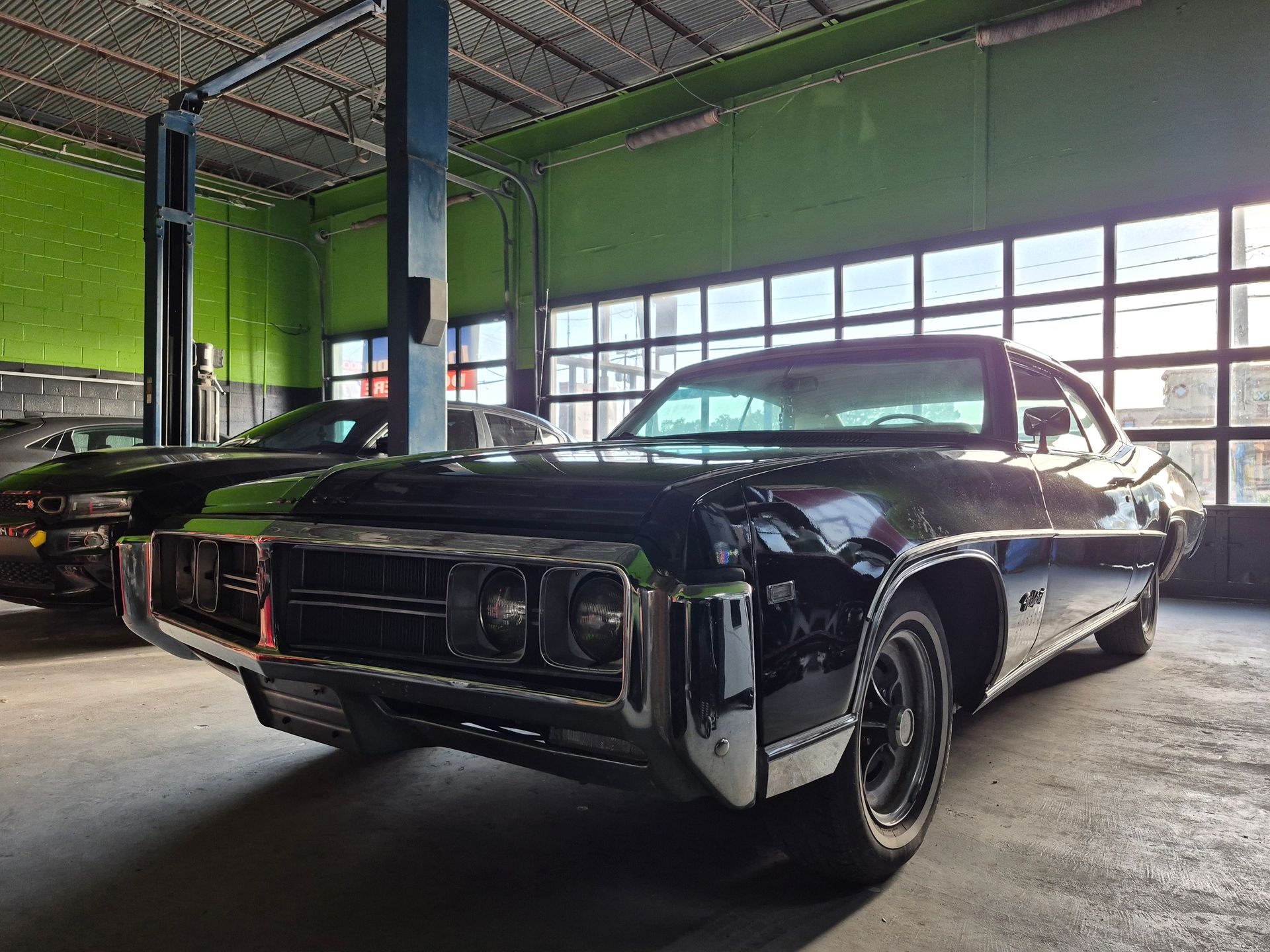 Black classic car in a garage, front view with chrome details and green walls in the background
