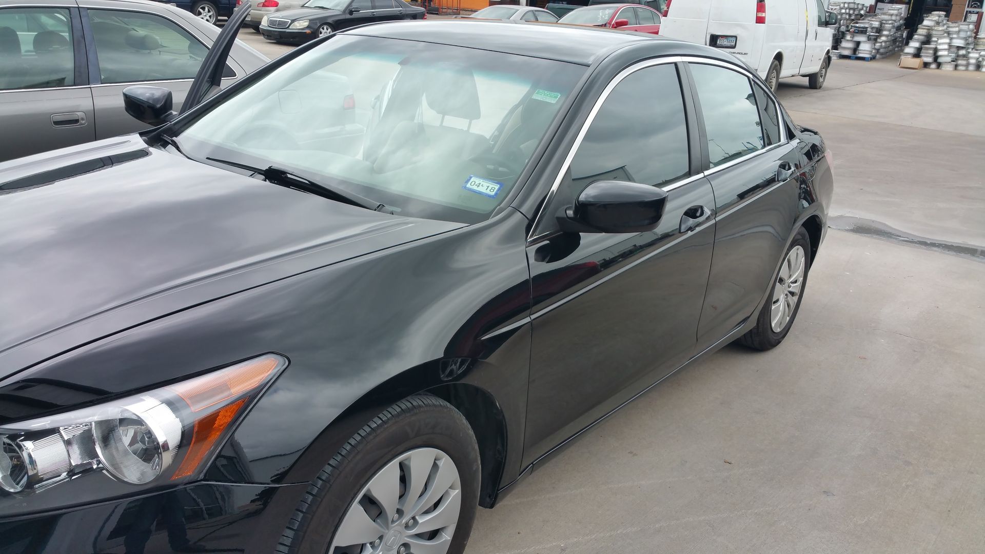 Black sedan parked in a lot, front-left view, with other cars in the background.
