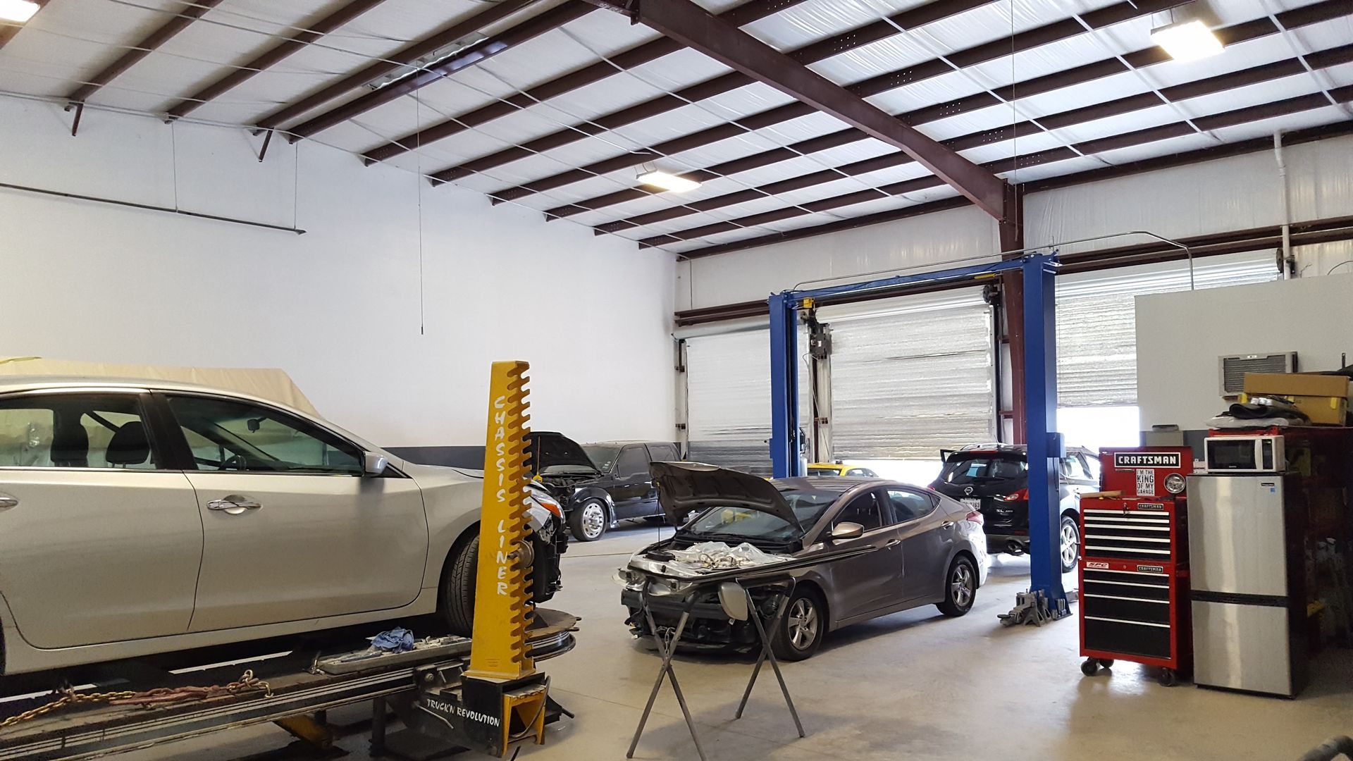 Auto repair shop with cars on lifts and one in the center bay under bright overhead lights