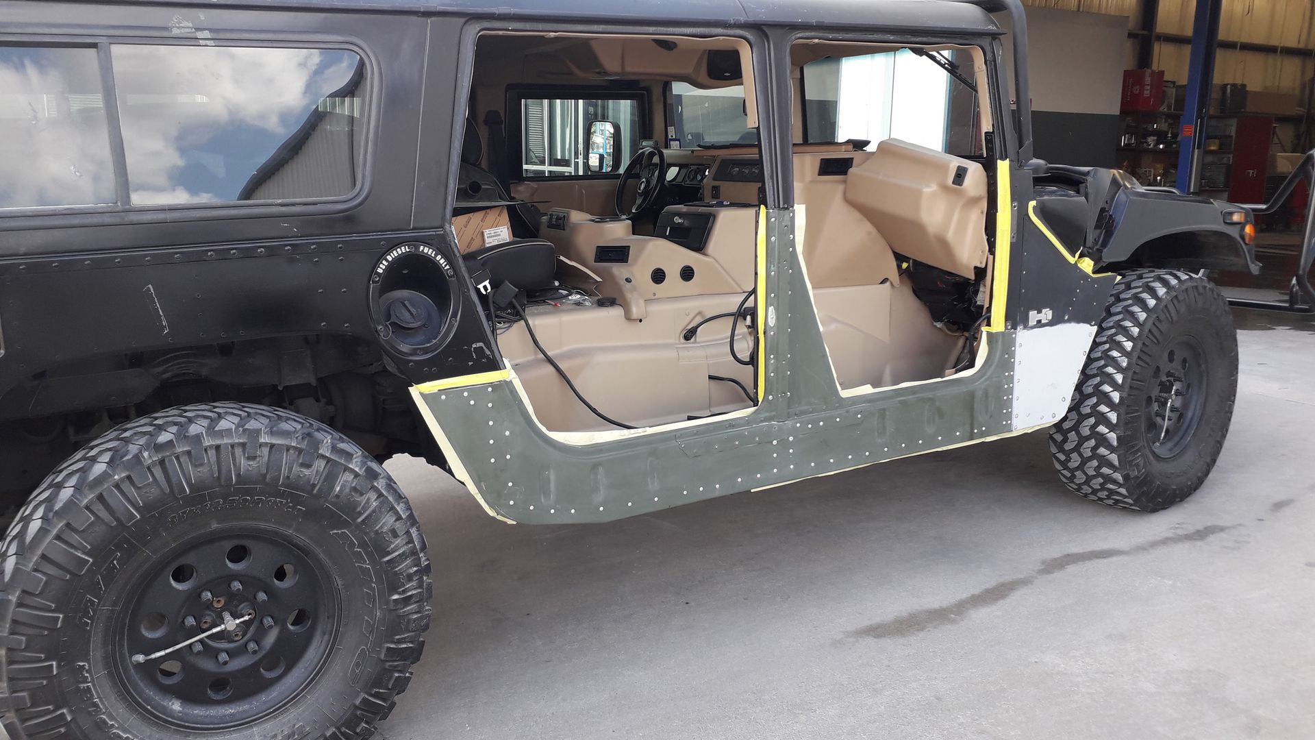 Black off-road Jeep with tan interior and doors removed, parked in a garage