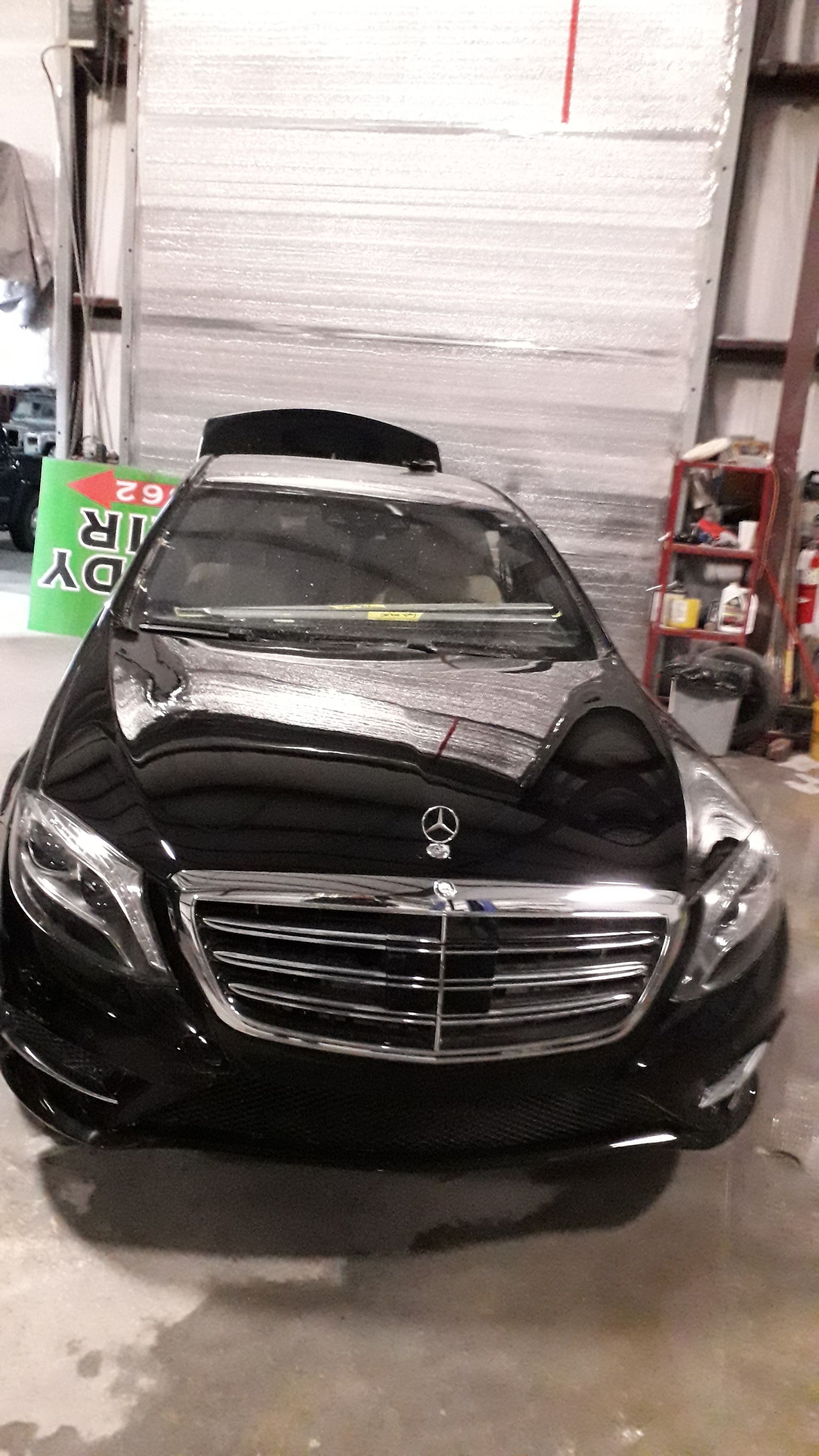 Black luxury sedan parked indoors in a garage, front view with chrome grille.