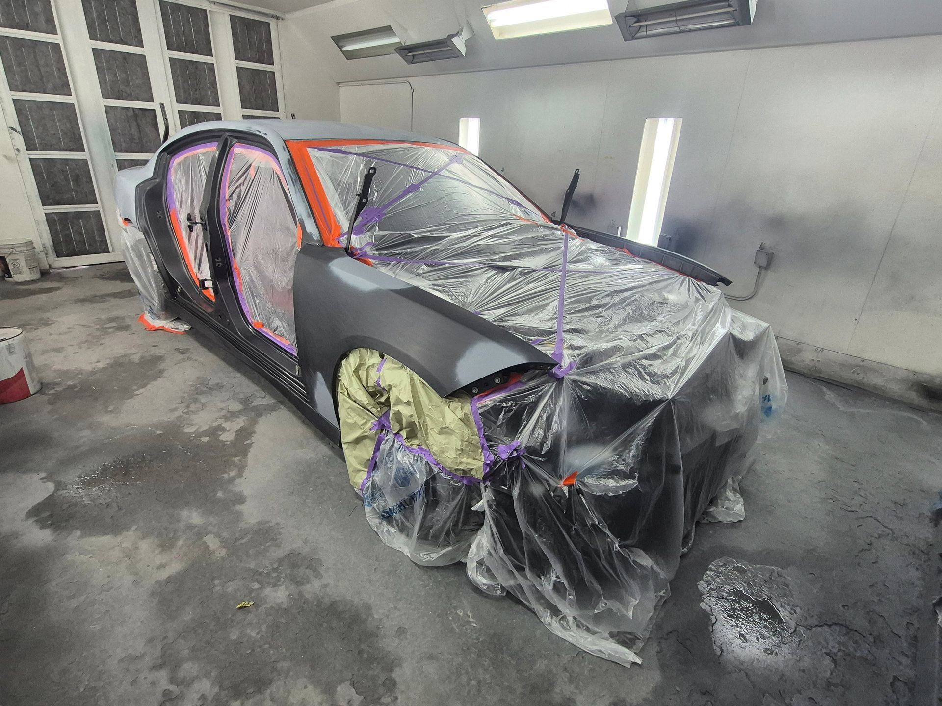 Damaged car in a spray booth, covered in plastic and primer for body repair