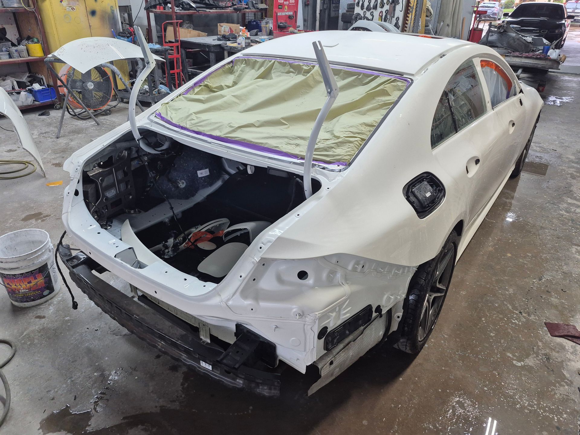Damaged white sedan in an auto body shop, rear and interior exposed during repair