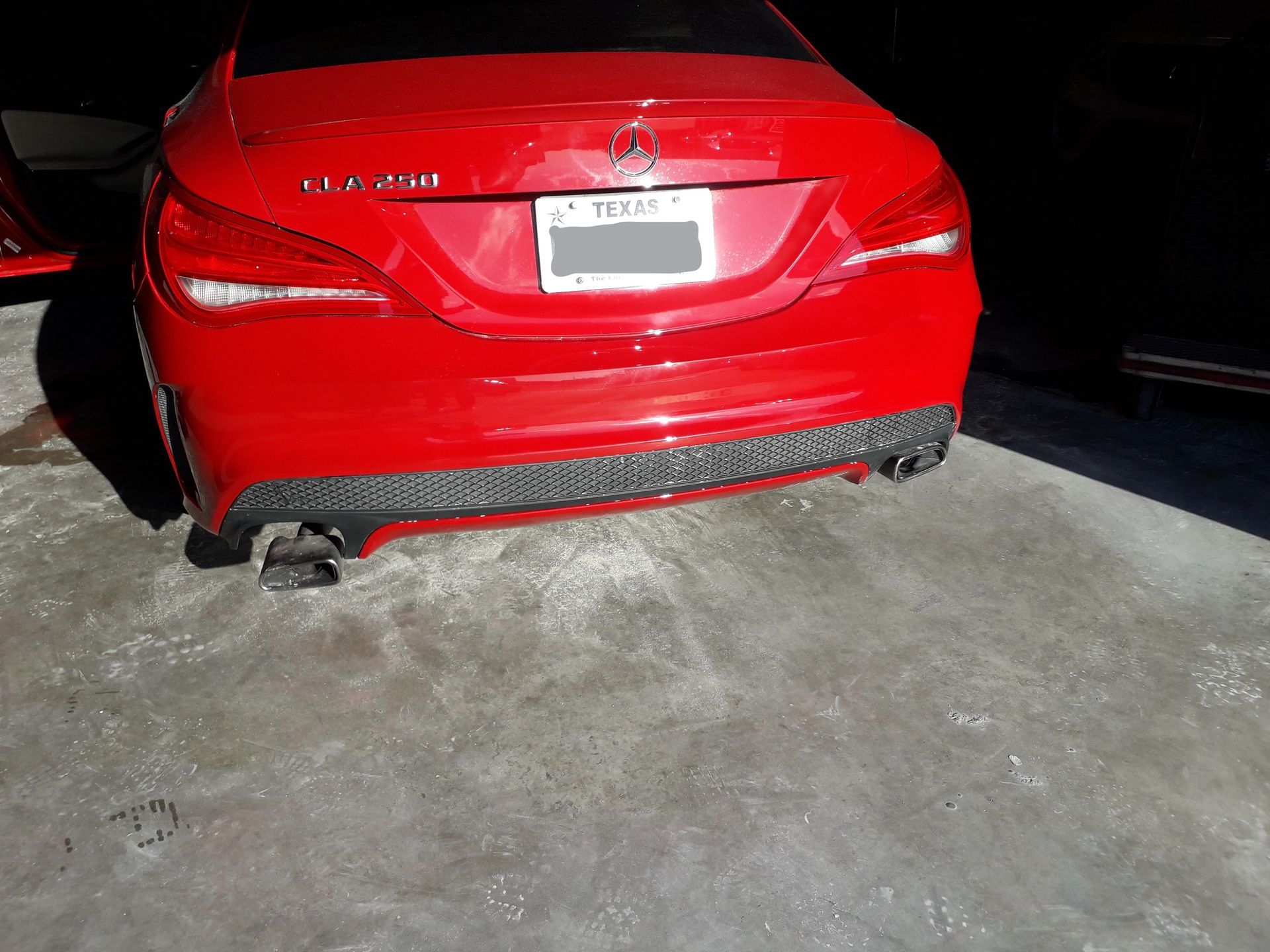 Red car parked in a garage, rear view, with visible exhaust and license plate area