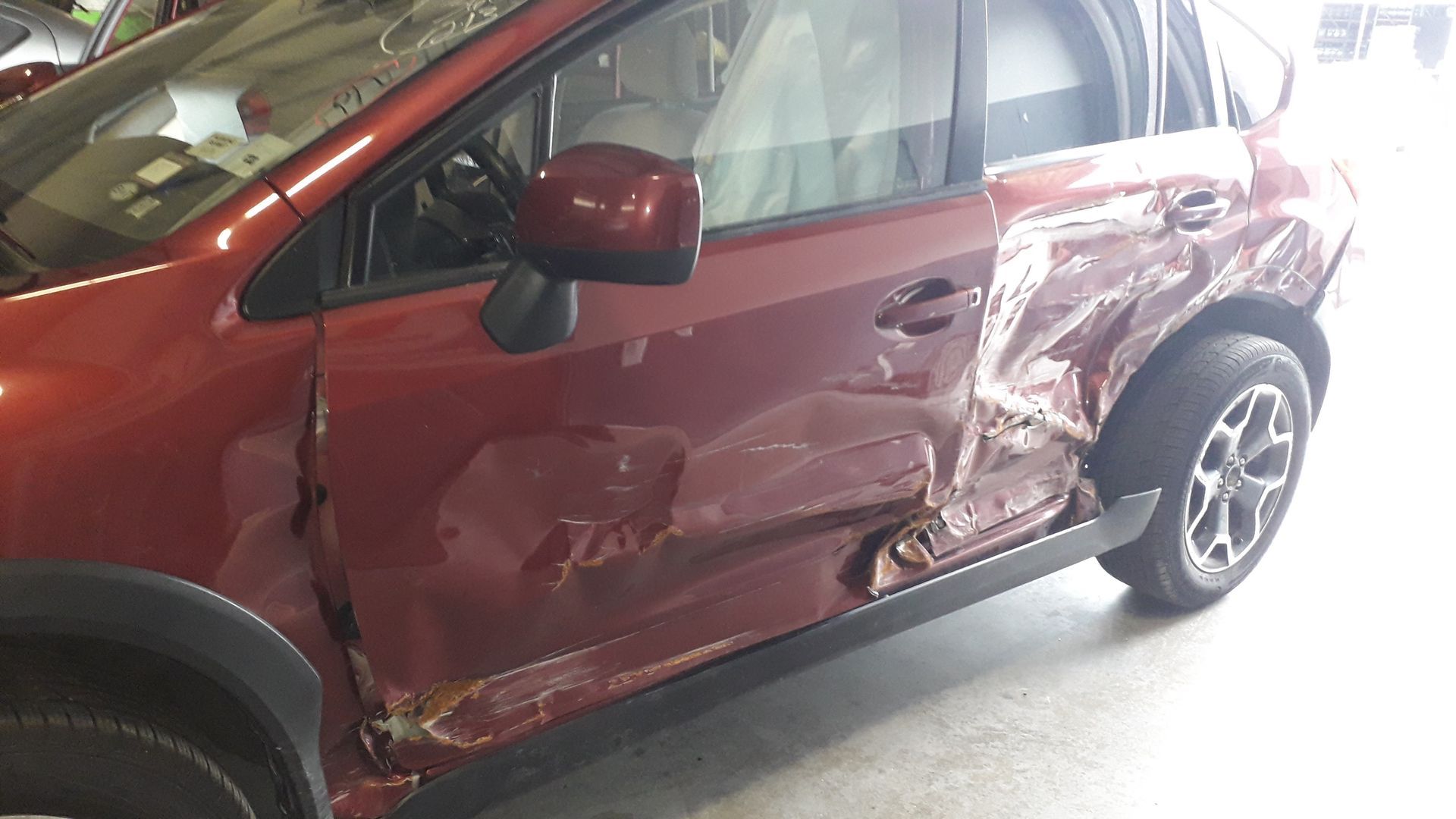Red SUV with heavy side damage and crushed rear door in a garage.