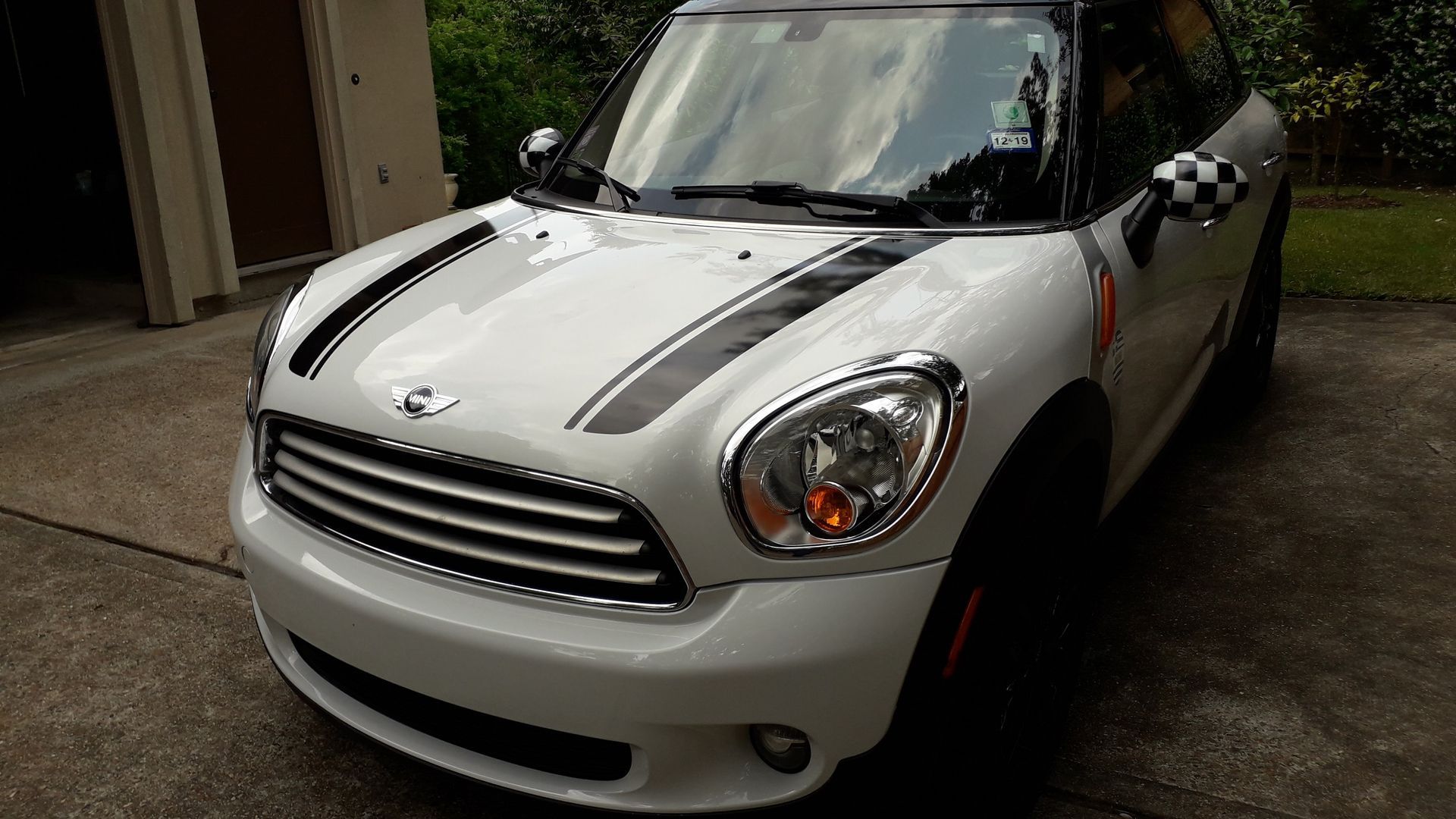 White Mini Cooper parked in a driveway, front view with gray racing stripes and red side mirror accents