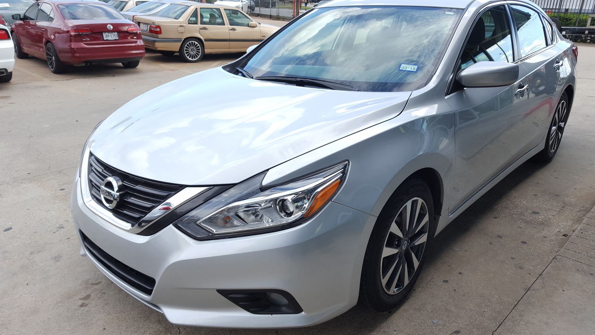 Silver Nissan sedan parked outdoors on a paved lot with other cars in the background