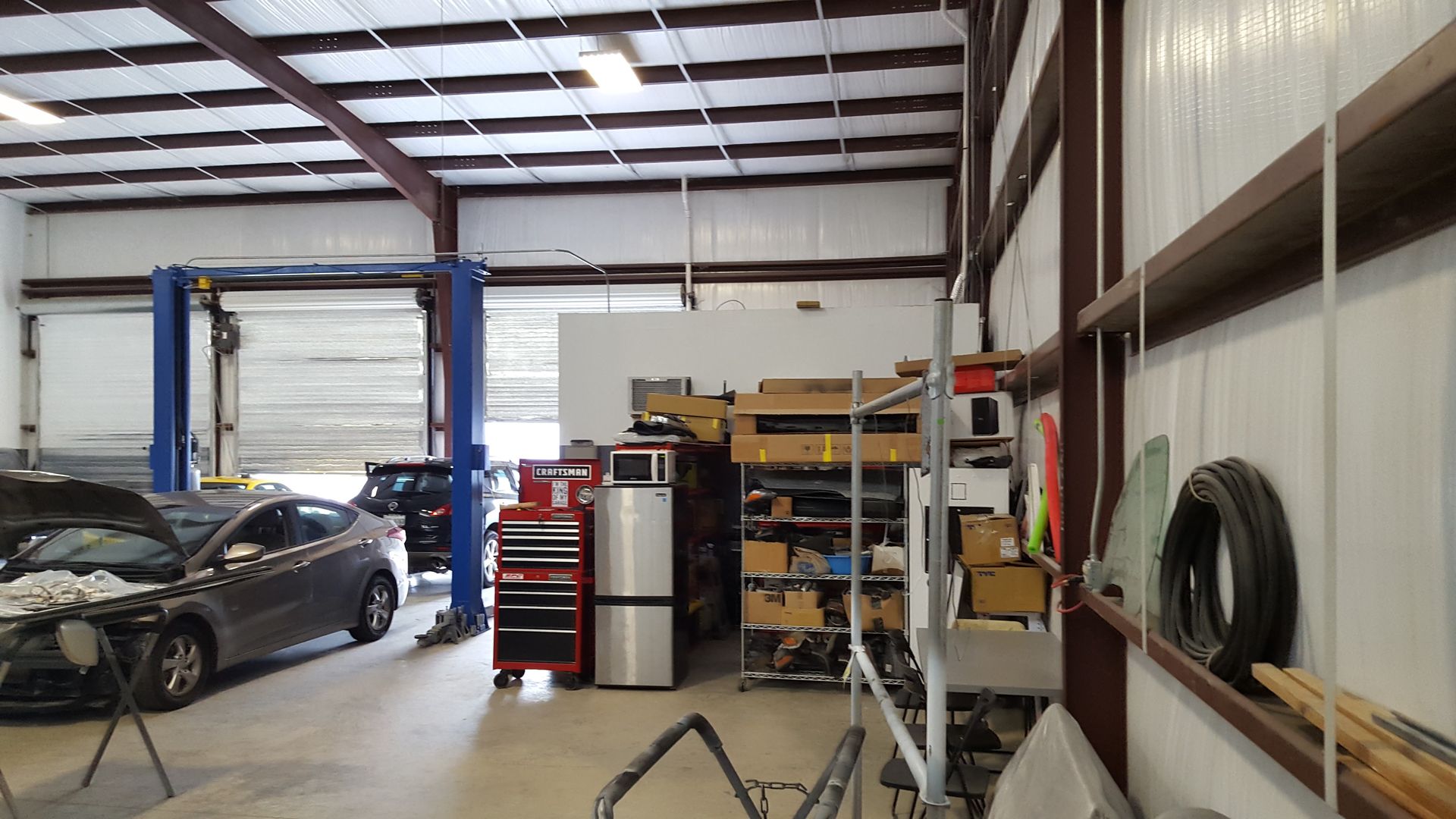 Auto repair shop interior with a black car, blue lift, and shelves of tools and equipment