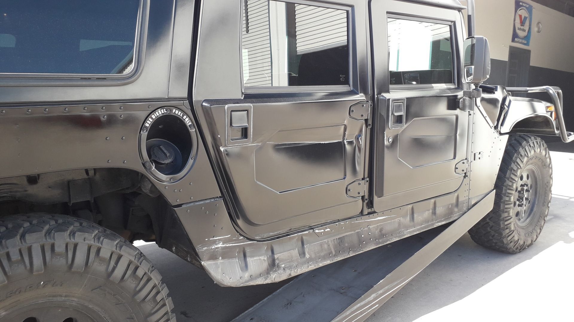 Black Hummer-style SUV with damaged side panel and missing fuel cap, parked on a street.