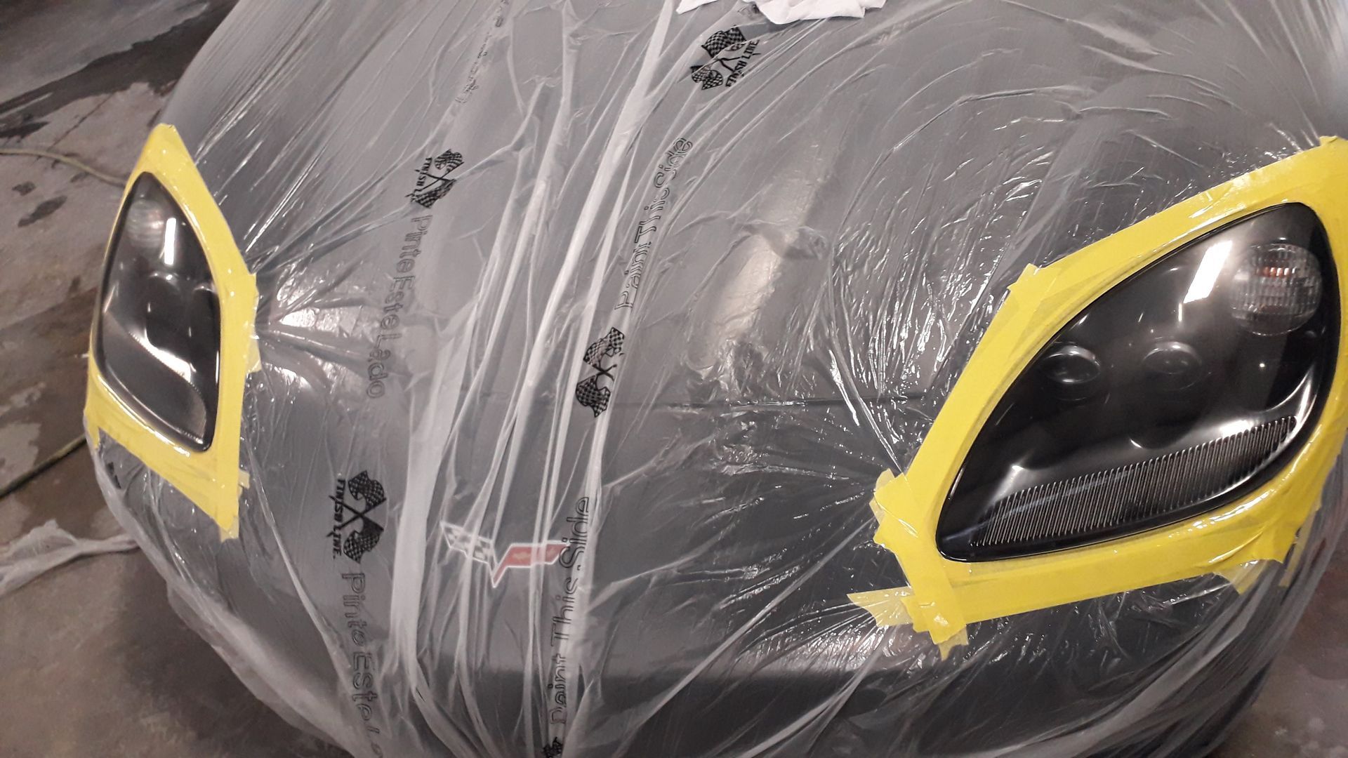 Close-up of a black car front covered in plastic, with yellow-taped headlight openings.