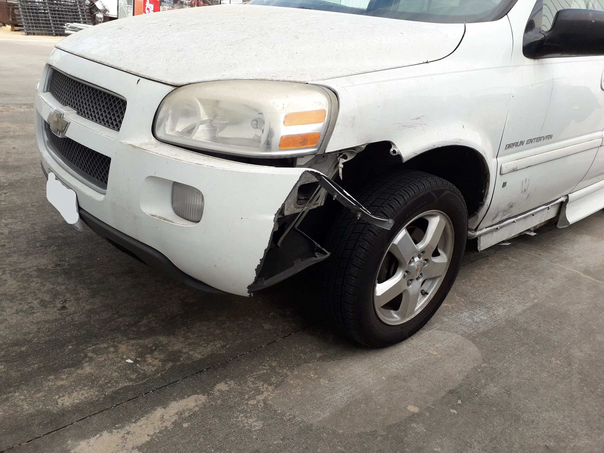 Damaged white SUV with a torn front-left fender and exposed wheel on a wet road