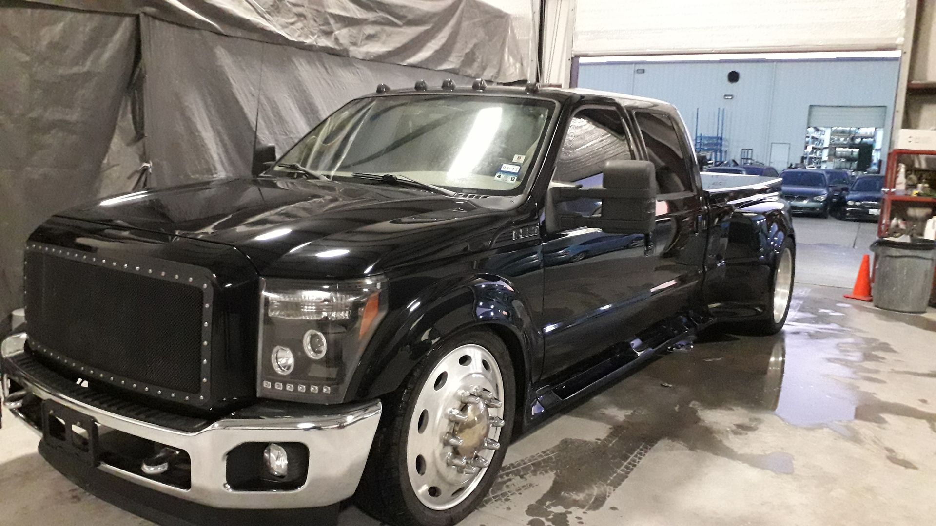 Black pickup truck parked indoors, with chrome grille and wheels, in a garage or workshop.