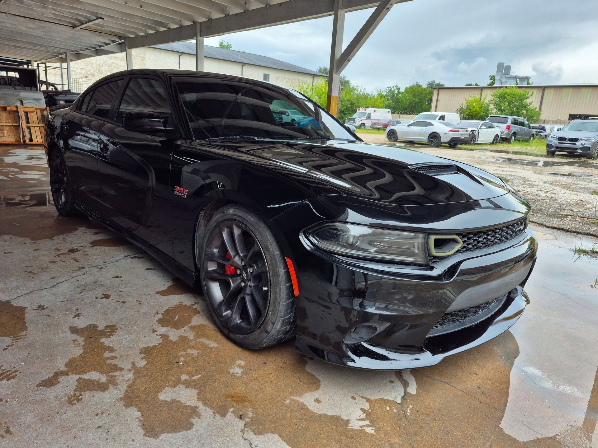 Black Dodge Charger parked under a canopy at a car wash, wet pavement around it.