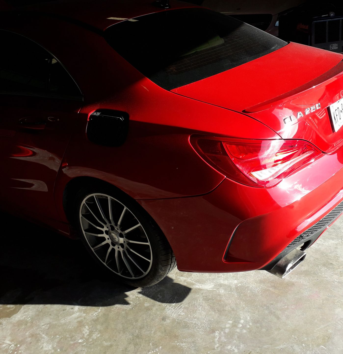 Red sports car parked in a garage, rear view with sunlight on the trunk and bumper.