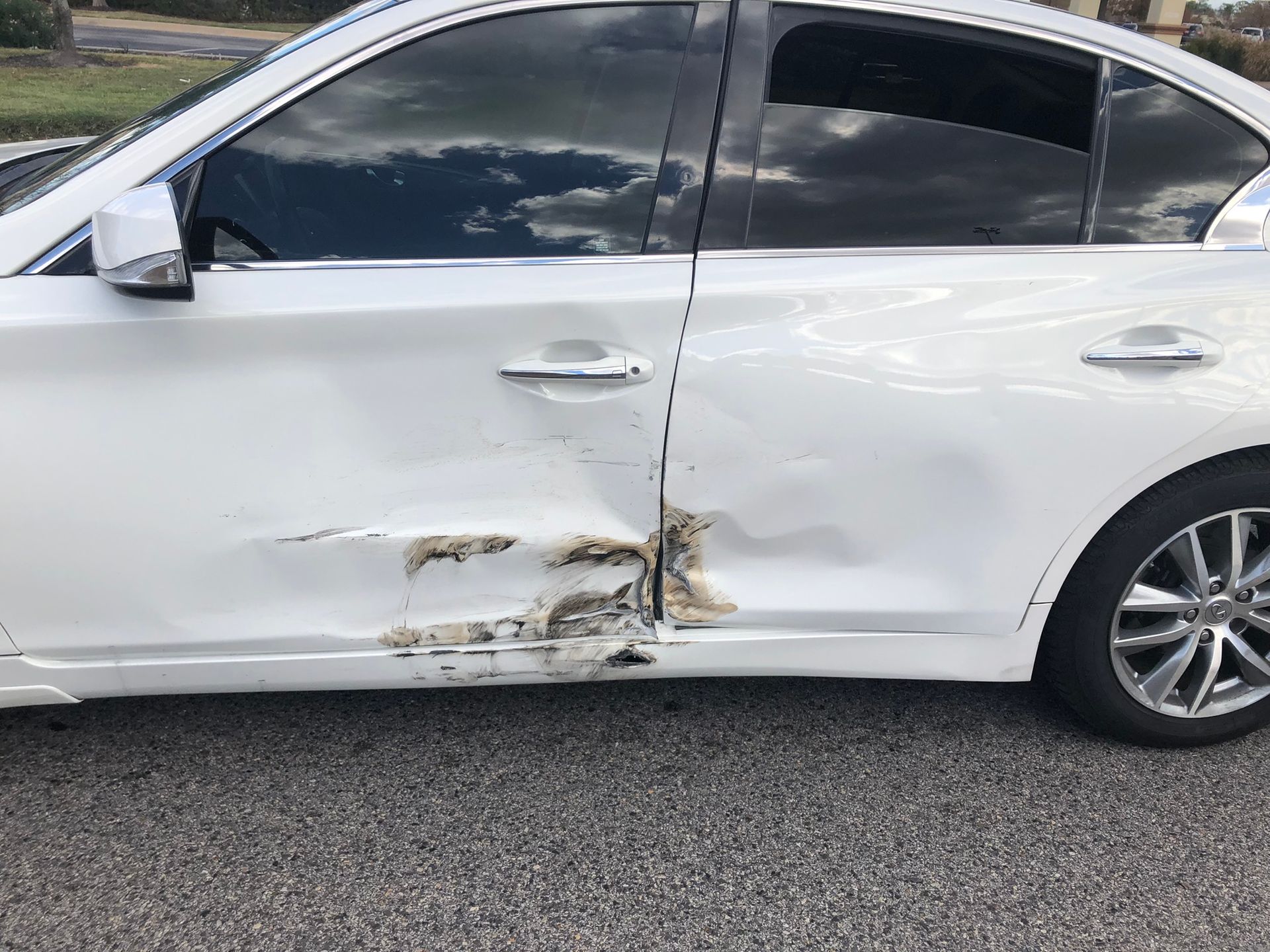 White sedan with severe dents and scrapes on the lower driver-side door and rocker panel.