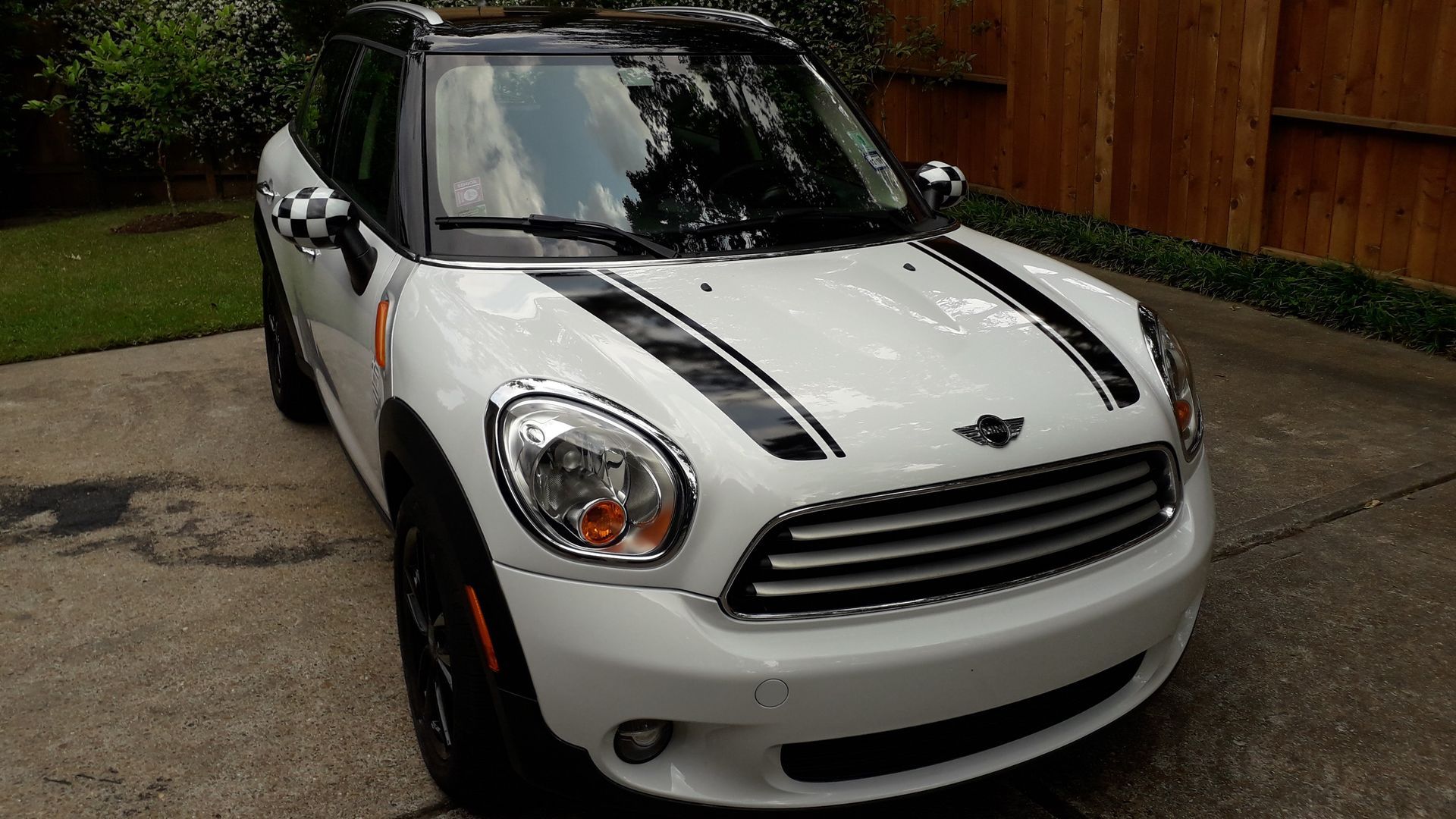 White Mini Cooper parked in a driveway, front view with black racing stripes and black roof