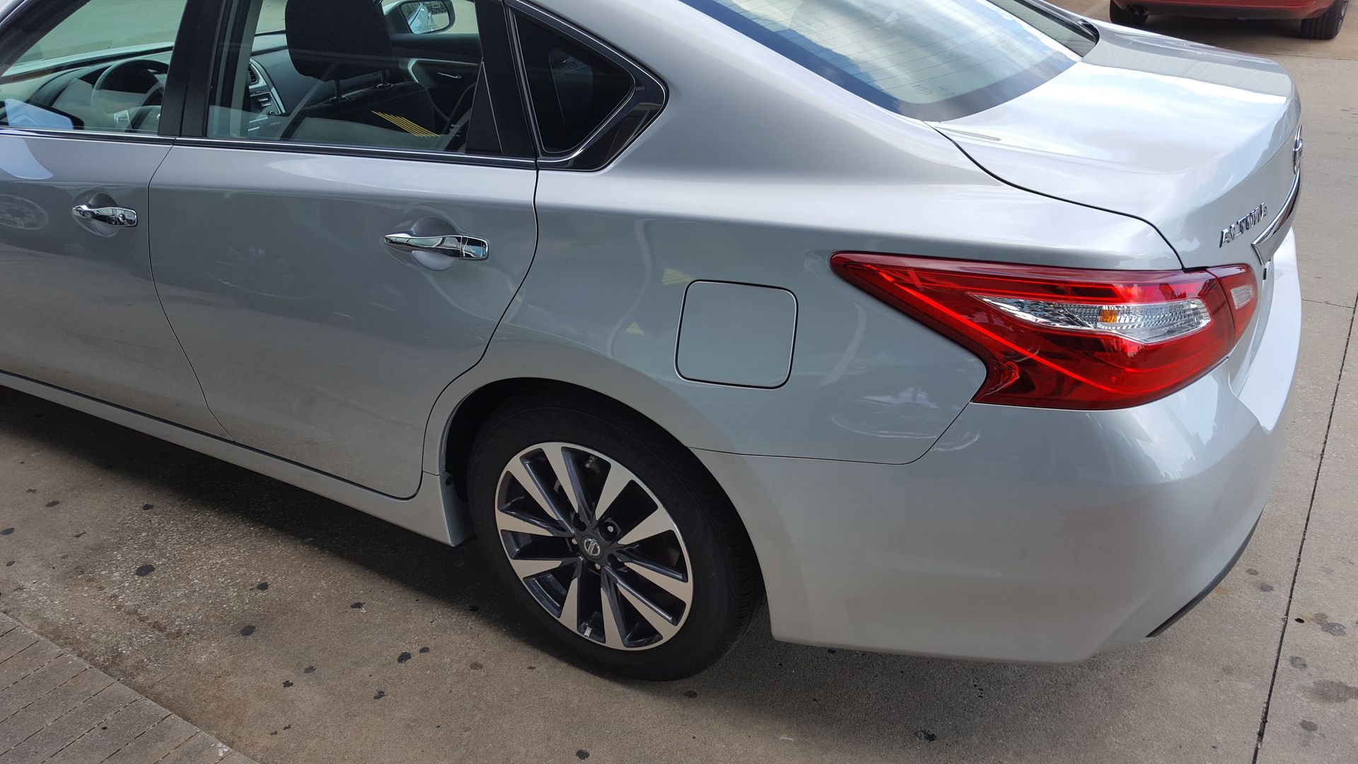 Silver sedan parked on a driveway, rear passenger side visible, with red taillights and a flat rear tire