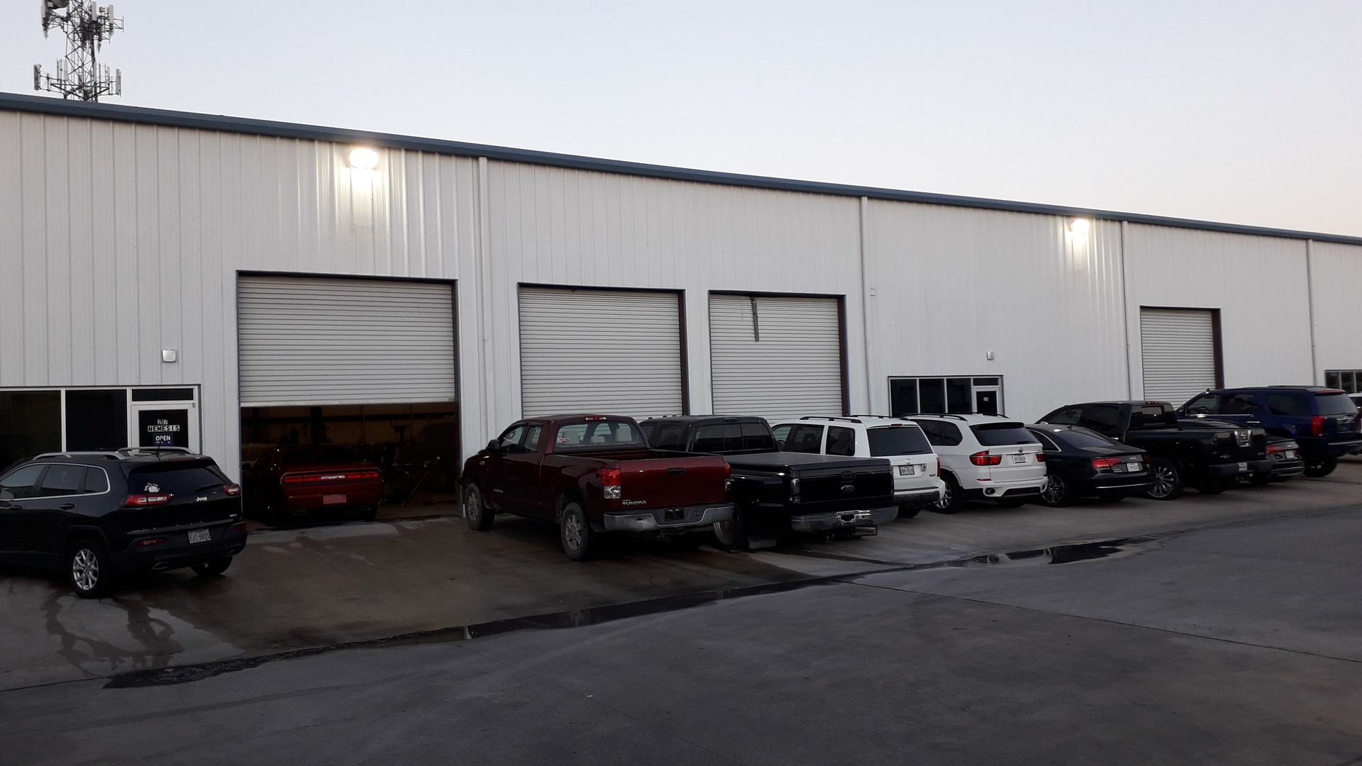 Row of parked cars outside a large white industrial building at dusk