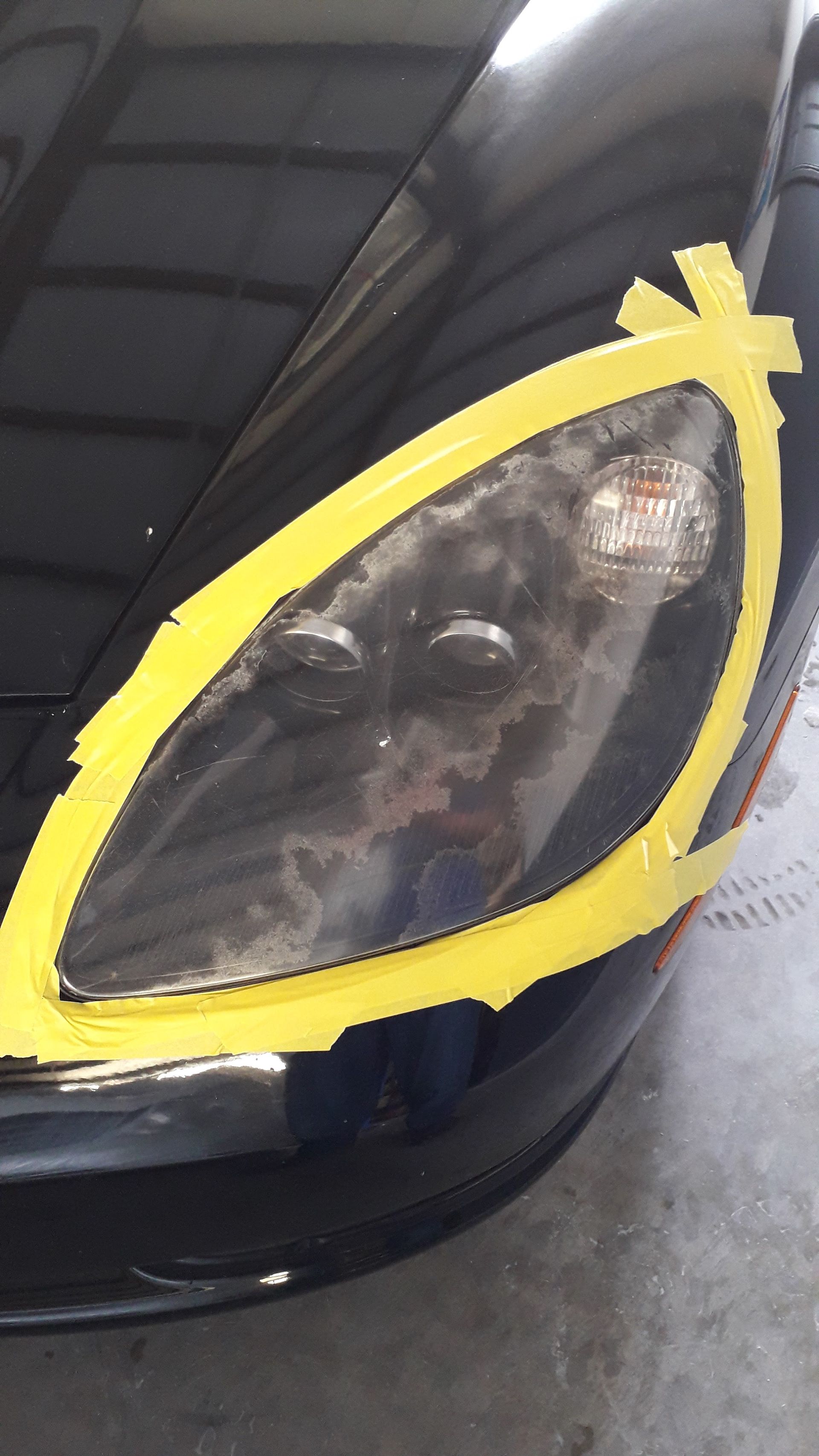 Close-up of a black car headlight outlined with yellow tape, showing damage and cracks