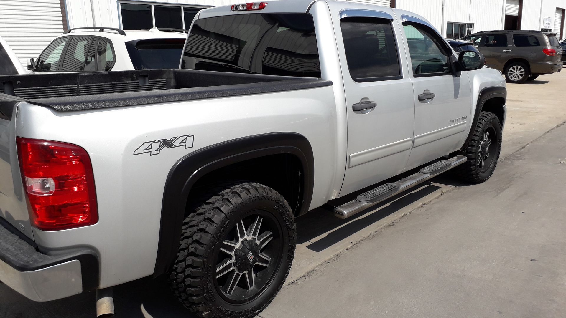 Silver Chevrolet pickup truck parked outdoors at a dealership, side view with black wheels and running boards