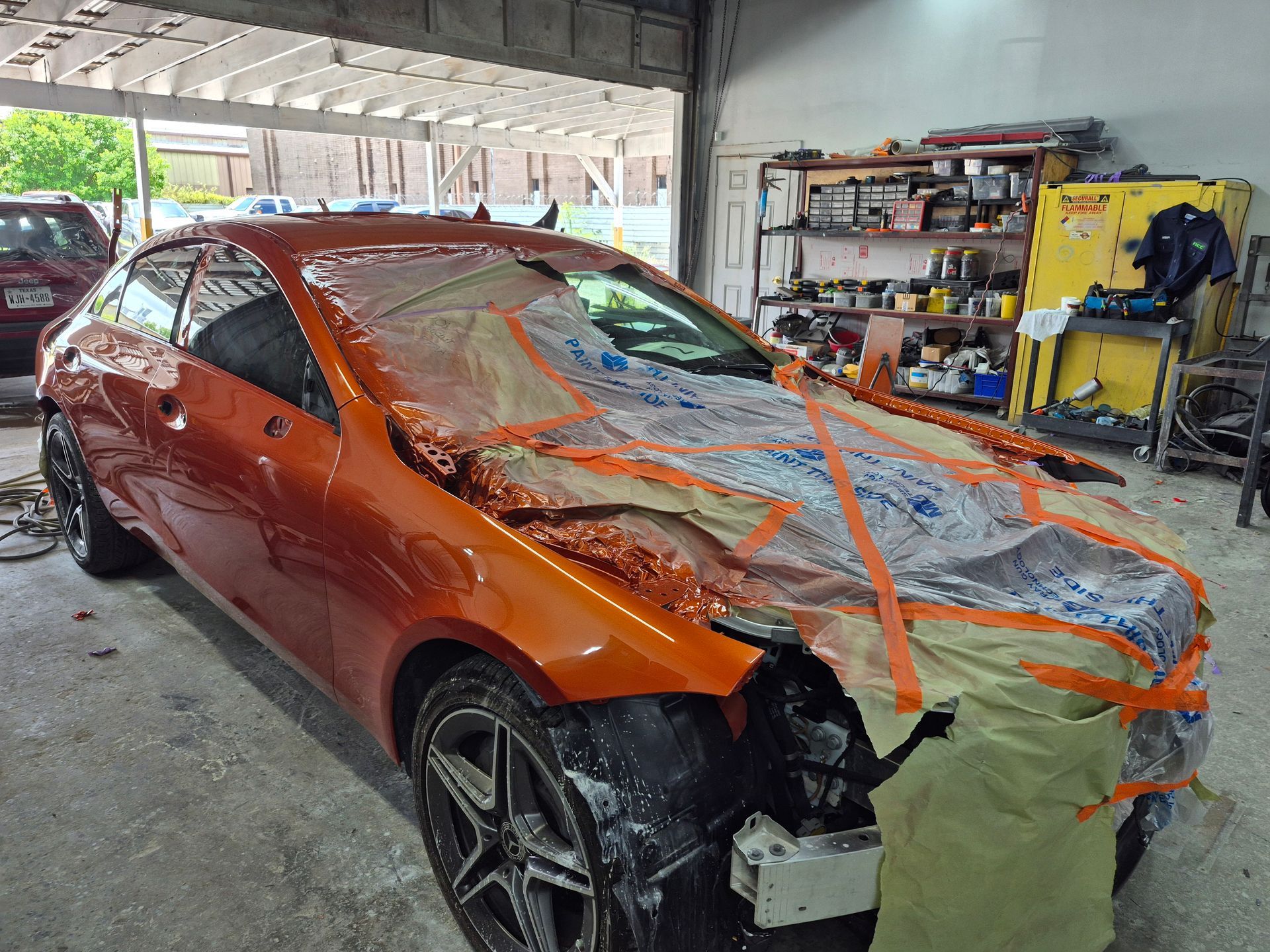 Orange car wrapped in masking tape and foil inside an auto repair shop