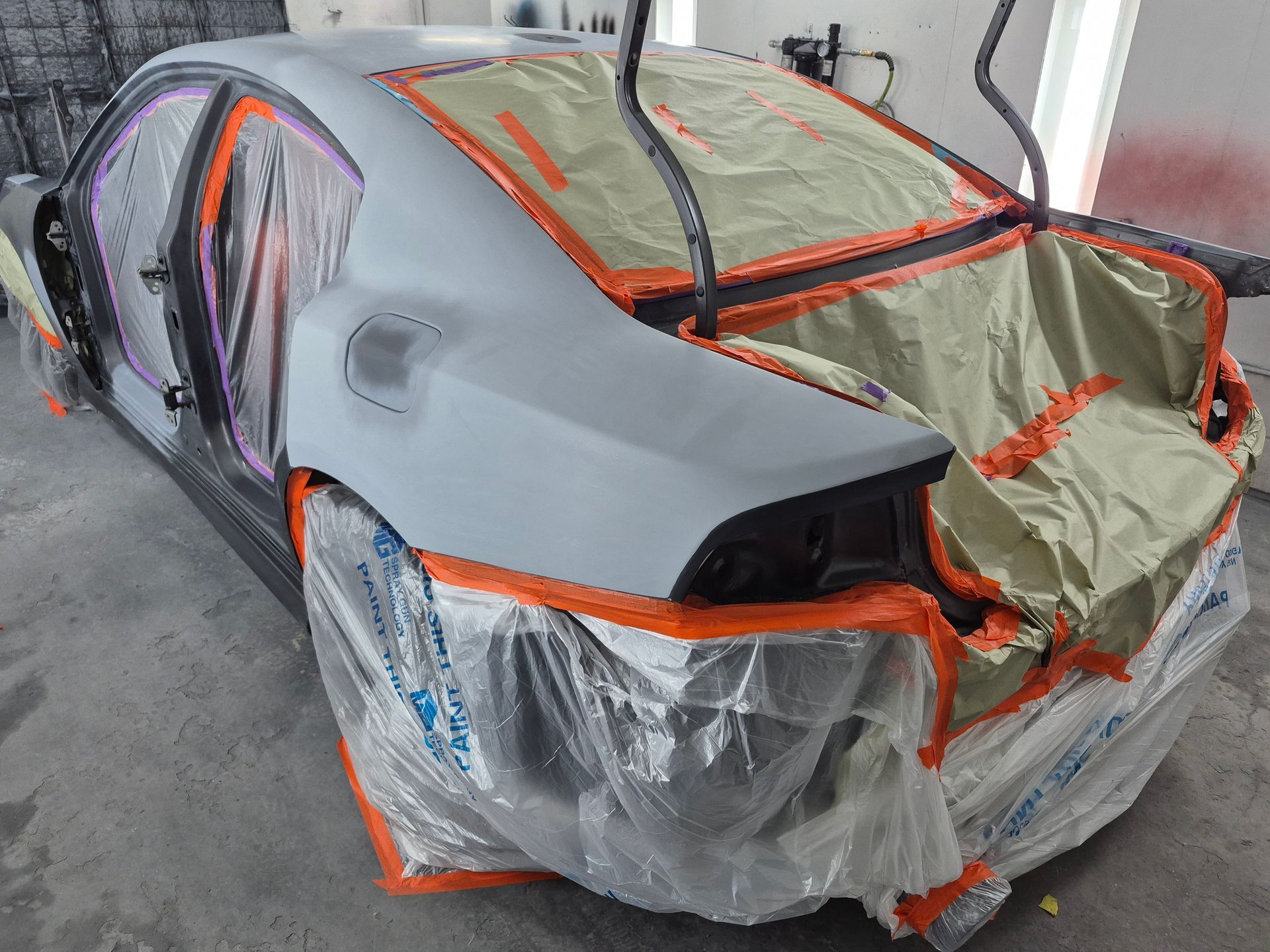 Partially wrapped silver car in a workshop, covered with plastic and orange tape for repair or painting