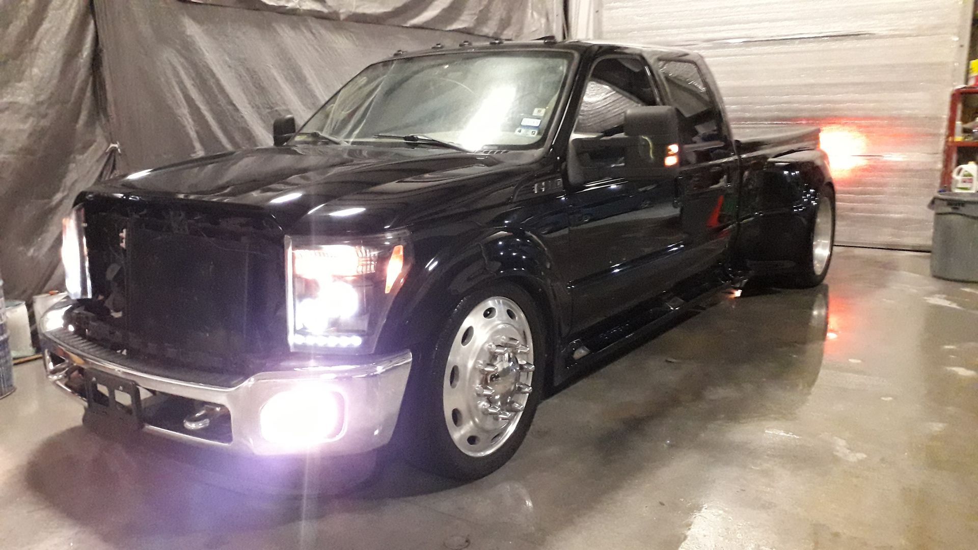 Black pickup truck with bright headlights parked indoors on a wet concrete floor