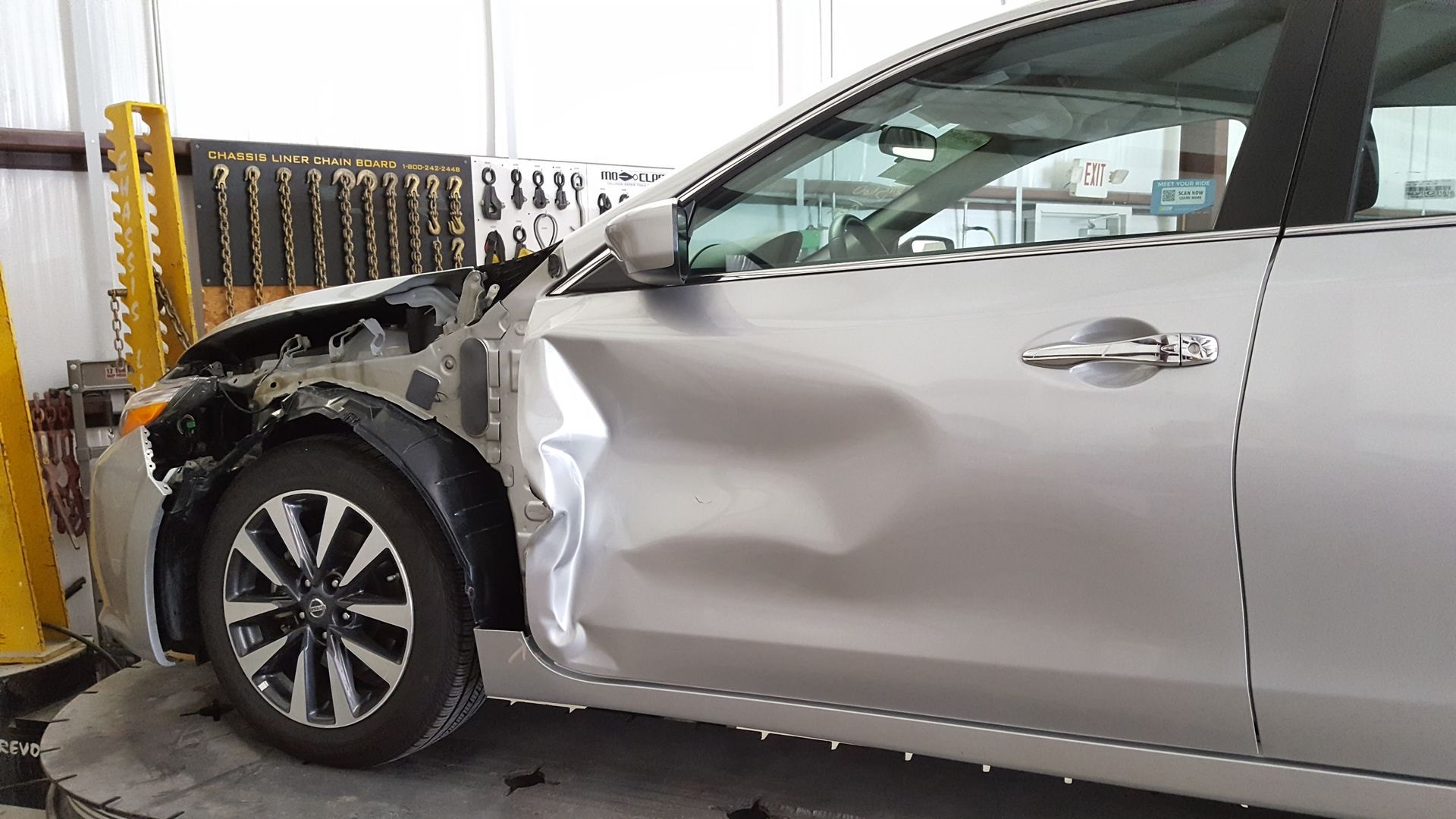 Silver sedan with crushed front-left fender in an auto repair shop