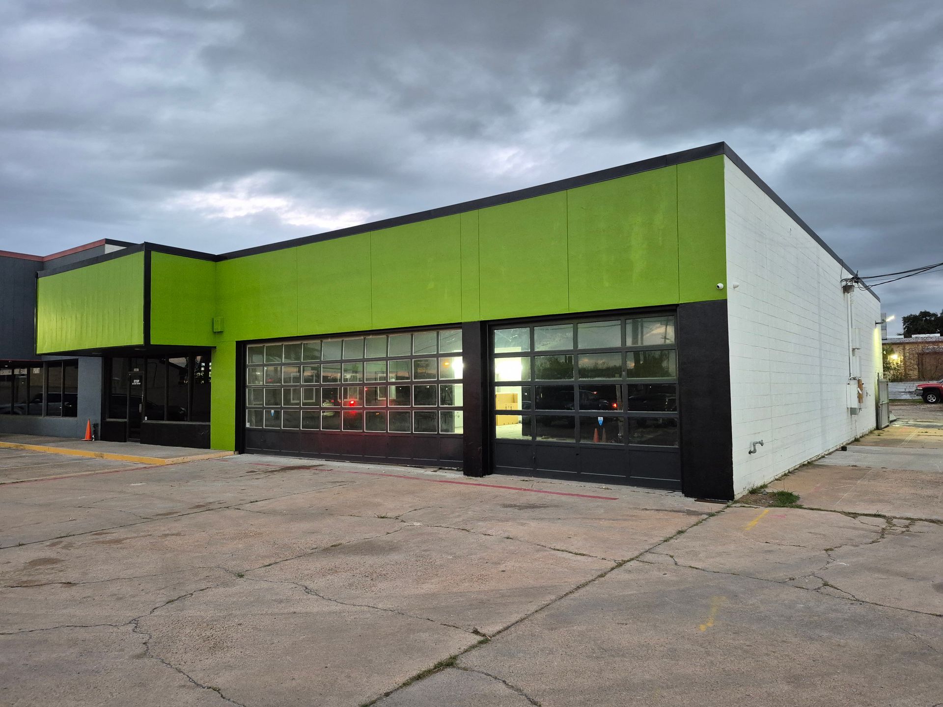 Green commercial building with black trim and large garage doors under a cloudy sky