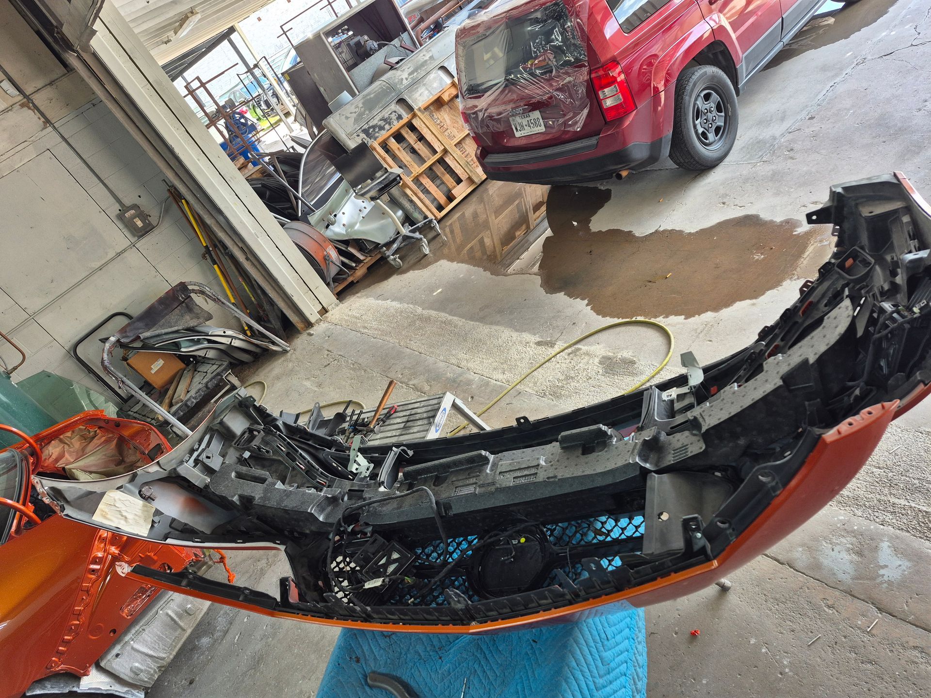 Damaged orange vehicle bumper in a garage, with a red SUV parked behind it.