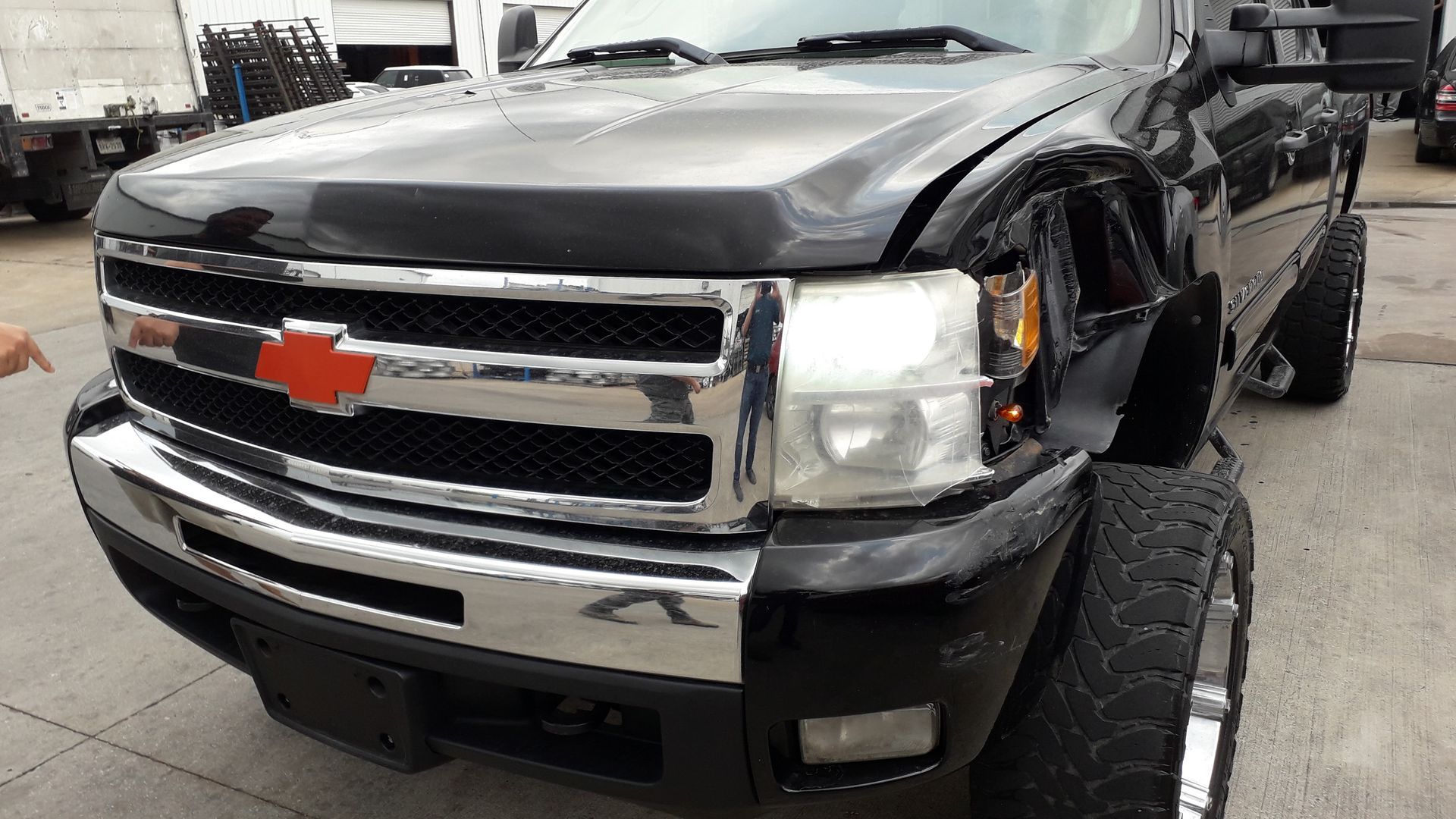 Damaged black Chevrolet pickup truck with front-end damage in a garage.