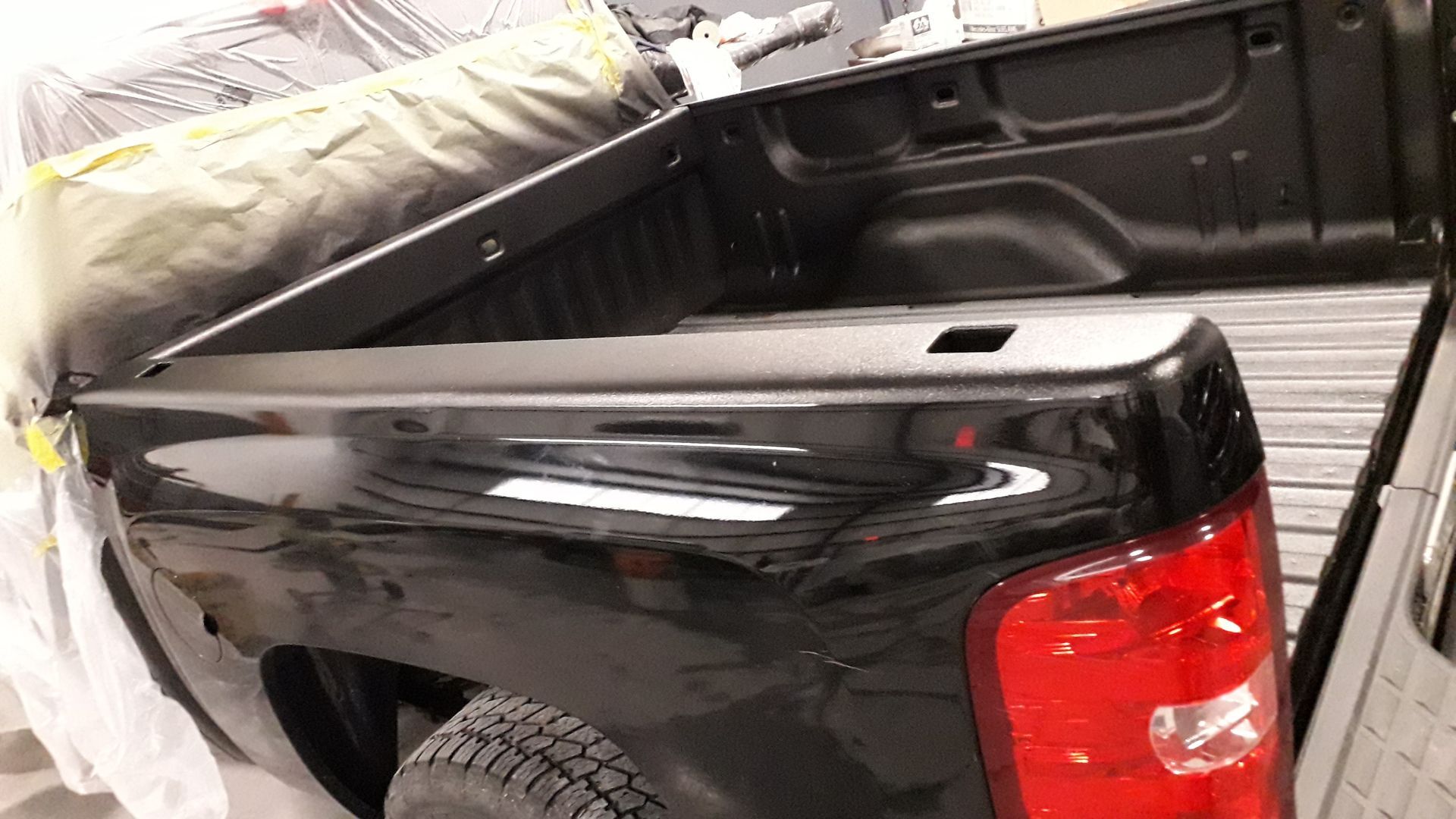 Black pickup truck bed with a red taillight, parked in a garage or workshop.