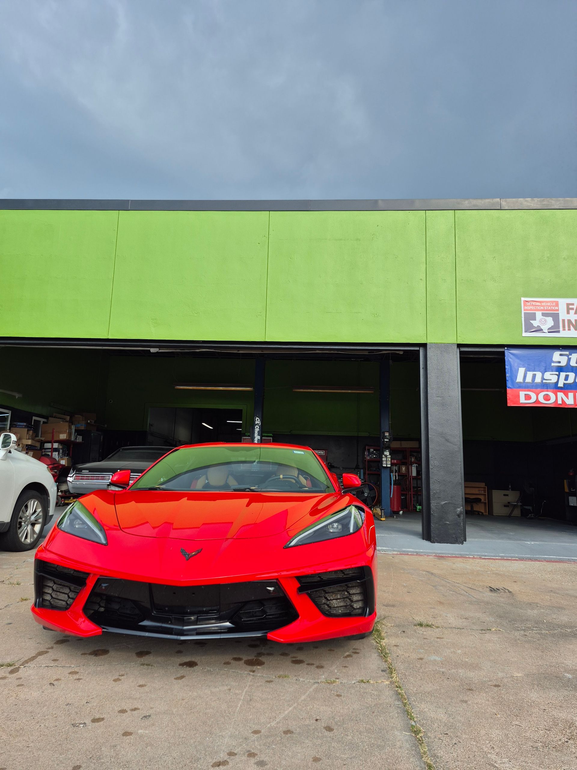Red sports car parked in front of a green auto shop garage.