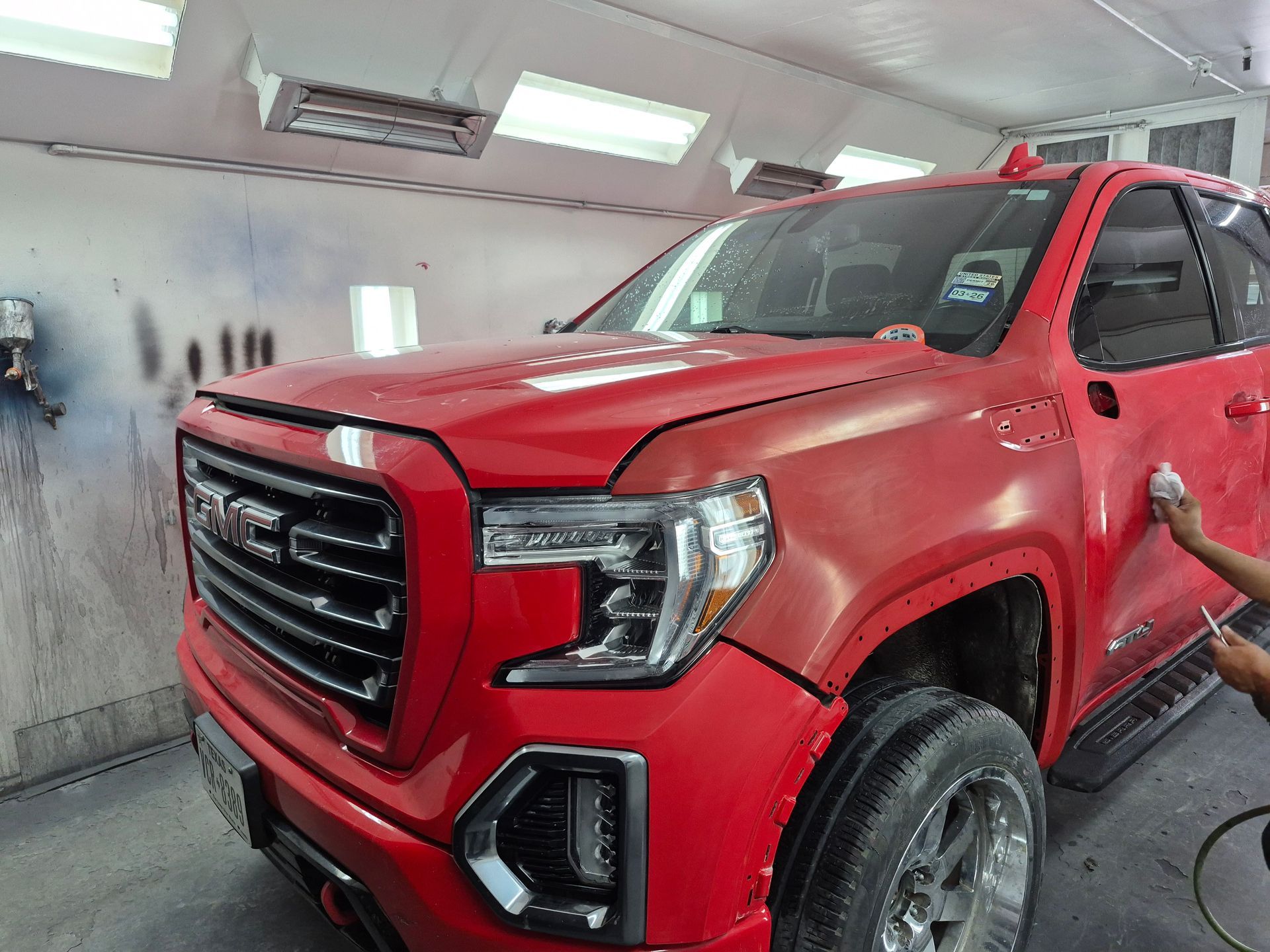 Red GMC pickup truck in a paint booth, with a person spray-painting the front fender