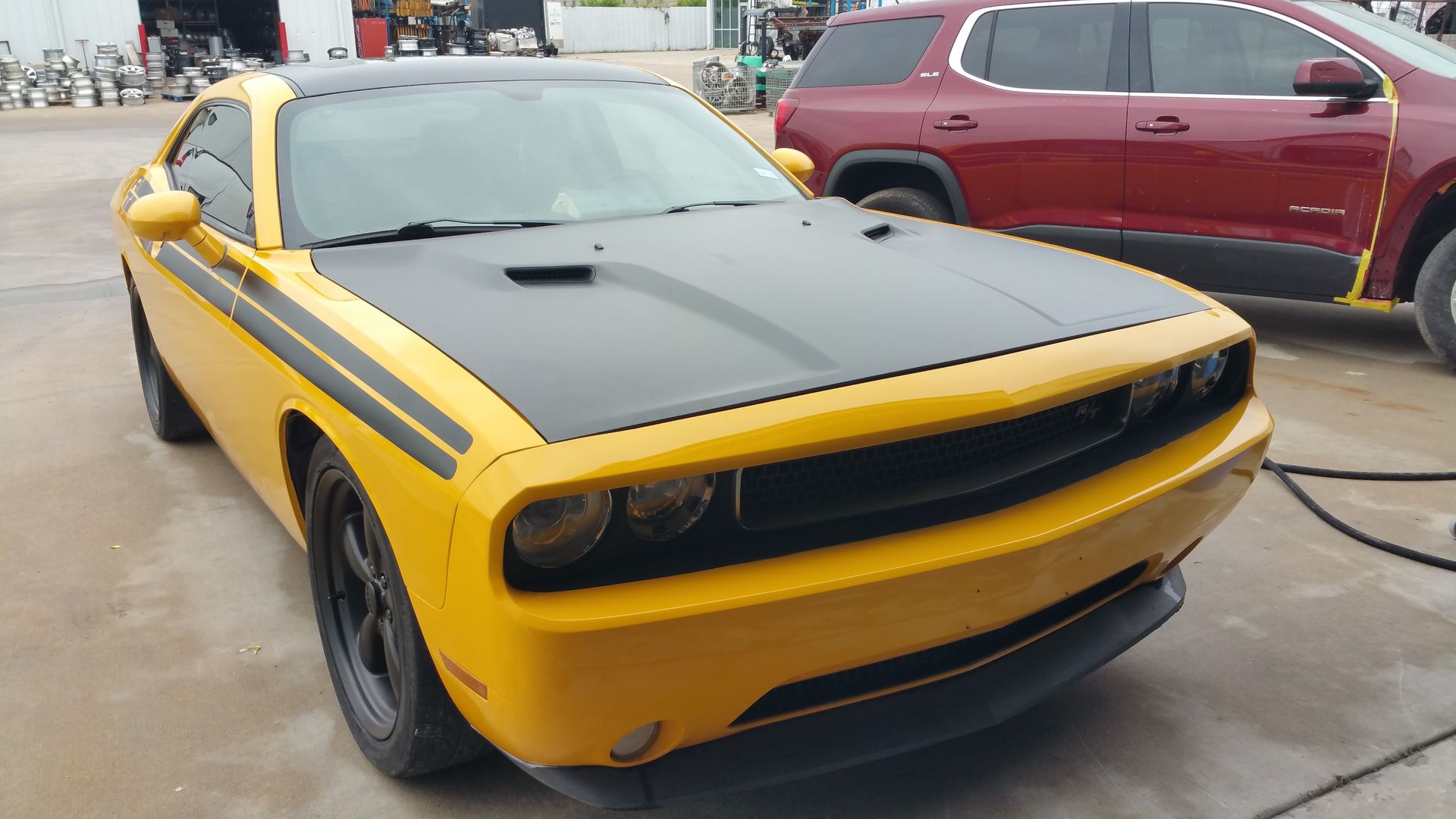 Yellow Dodge Challenger with black hood and stripes parked outdoors at a car meet