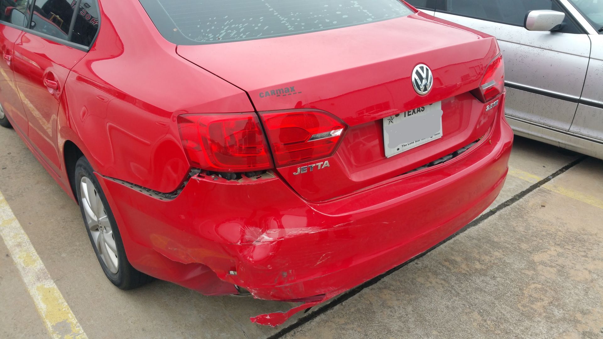Rear view of a red Volkswagen sedan with rear bumper damage in a parking lot