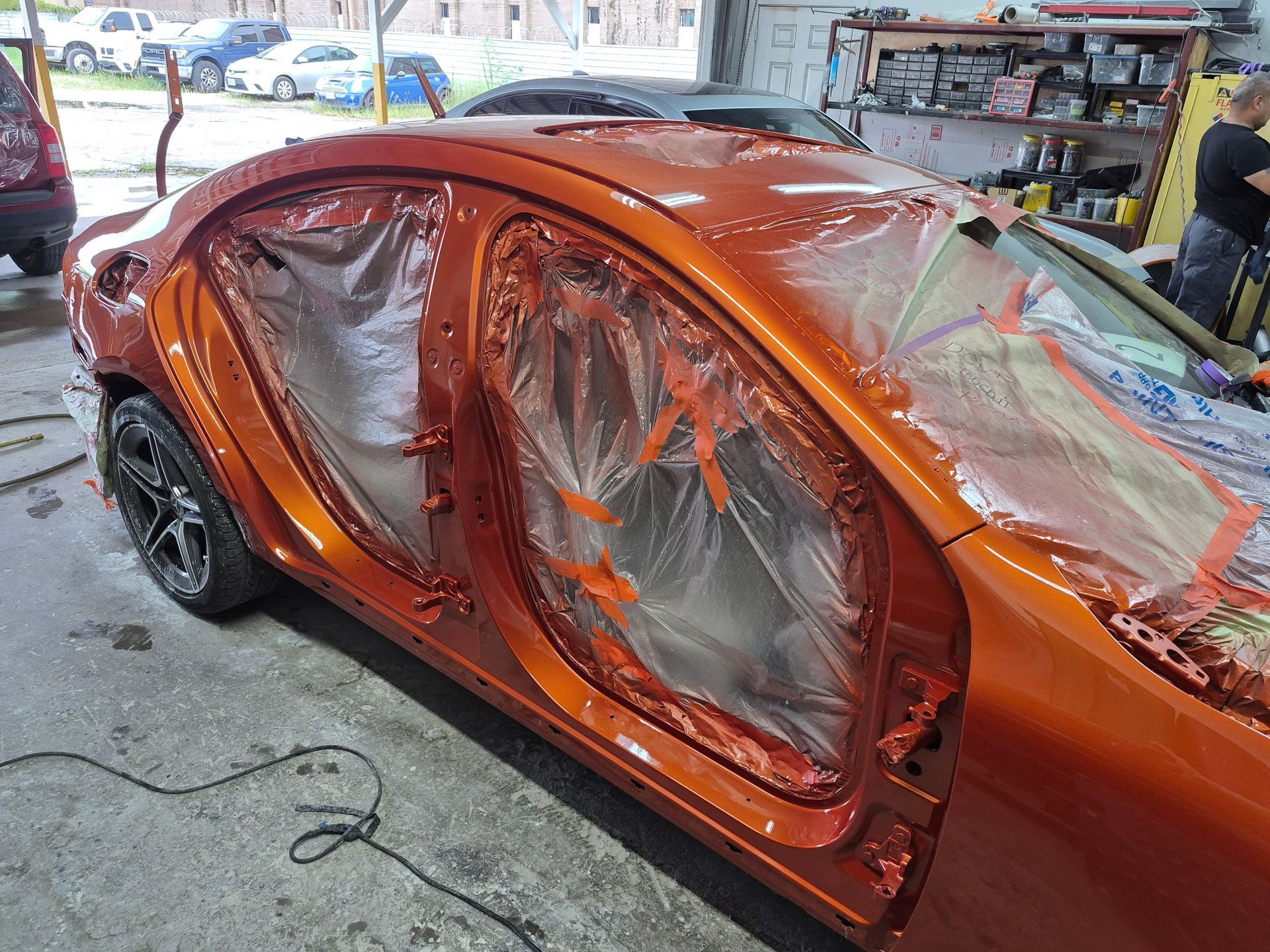 Orange car in a workshop, with doors and windows masked off for painting.