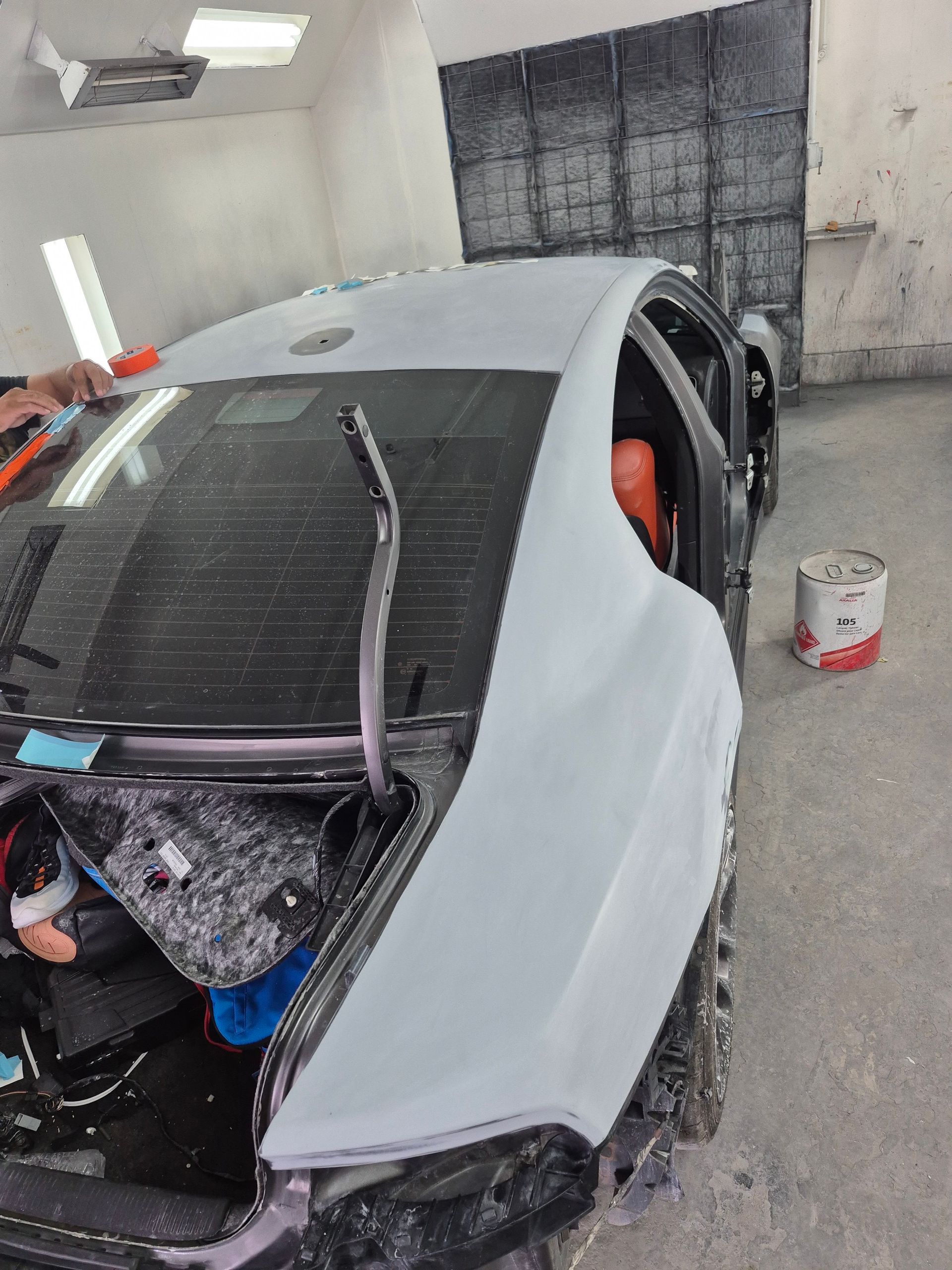Silver car in a garage with the windshield removed and front end disassembled during repair