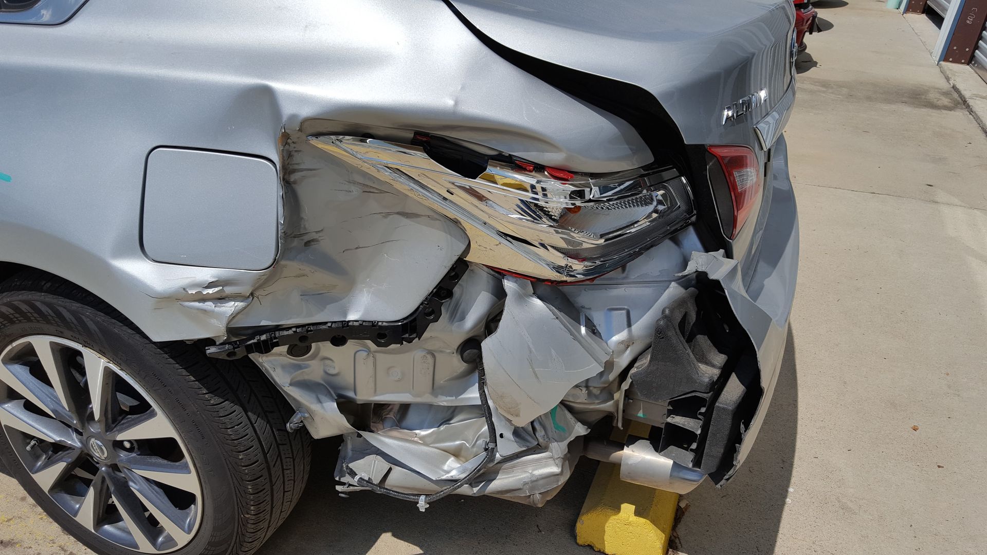 Severely damaged silver car rear-end collision with crushed bumper and exposed internal parts