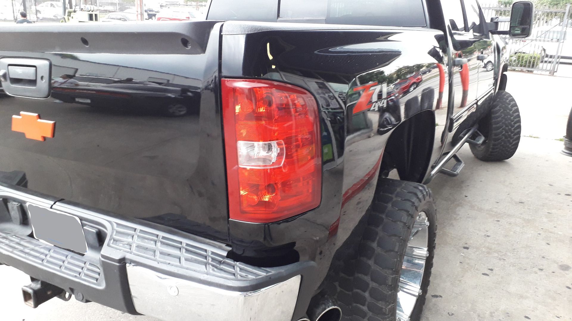 Black Chevrolet pickup truck with a large lifted suspension and oversized off-road tires, rear view in a lot