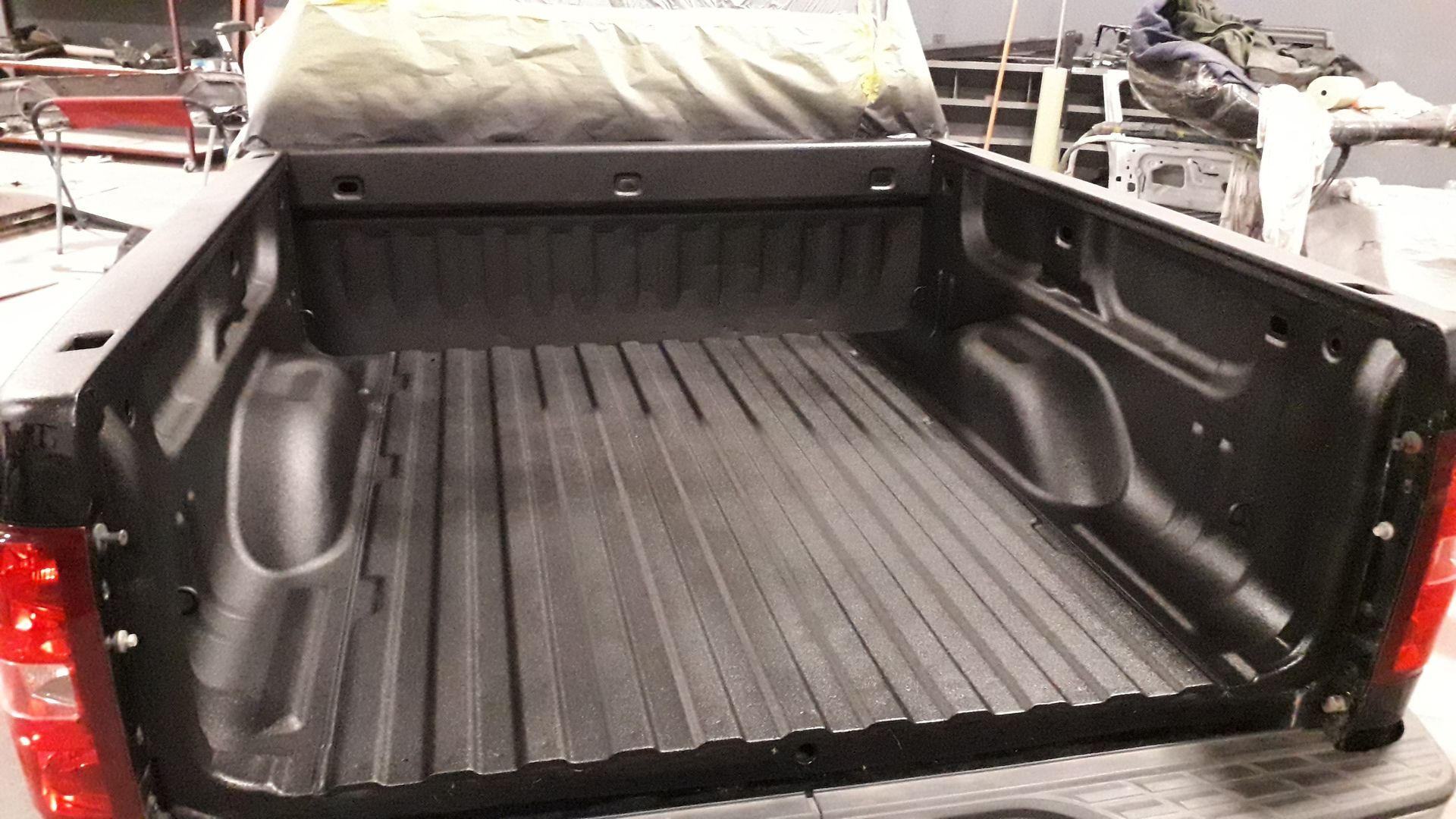 Truck bed lined with black spray-on coating, with a rolled cover at the cab end.