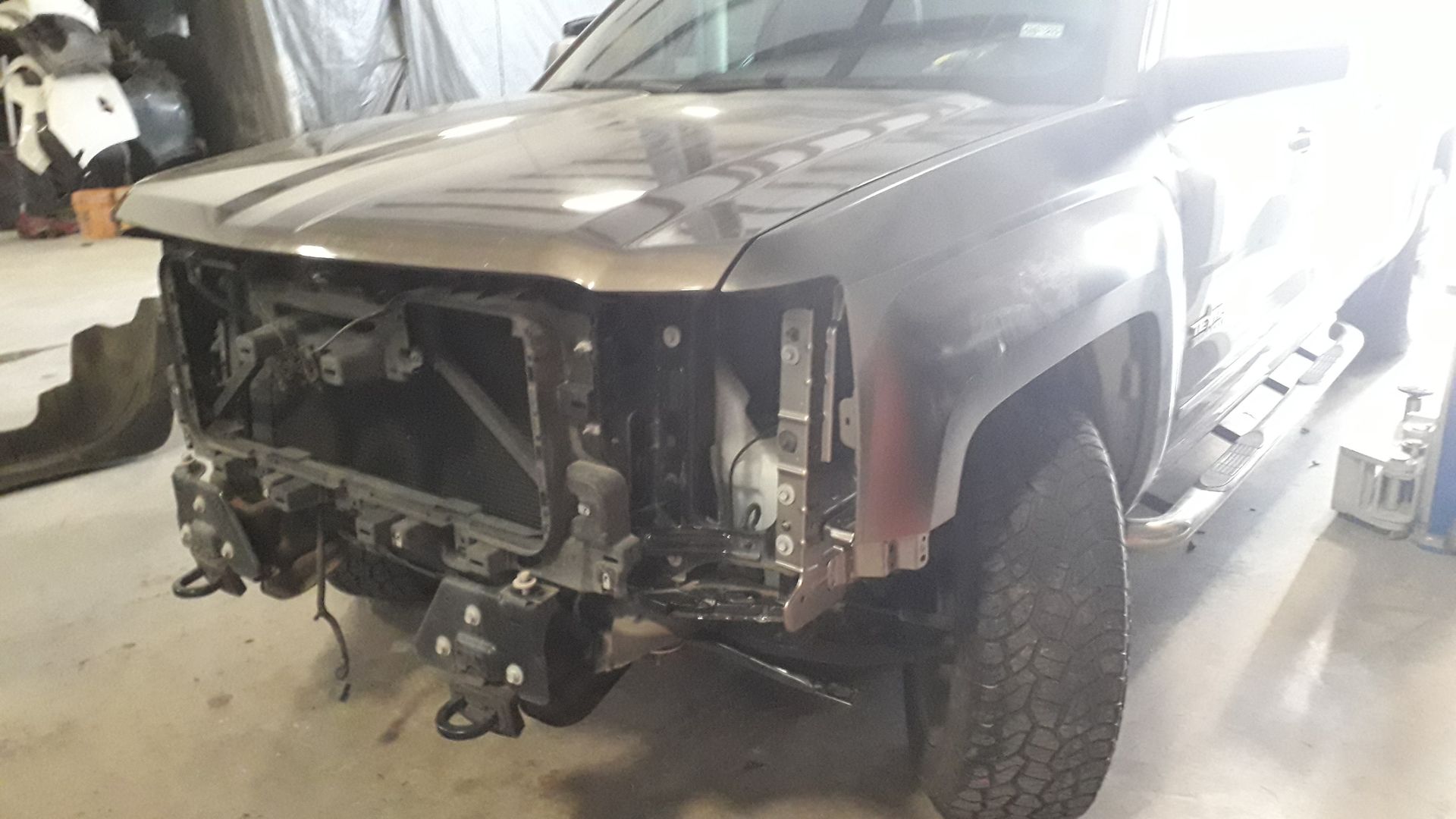 Damaged pickup truck with front end removed in a garage, exposed engine and headlights.
